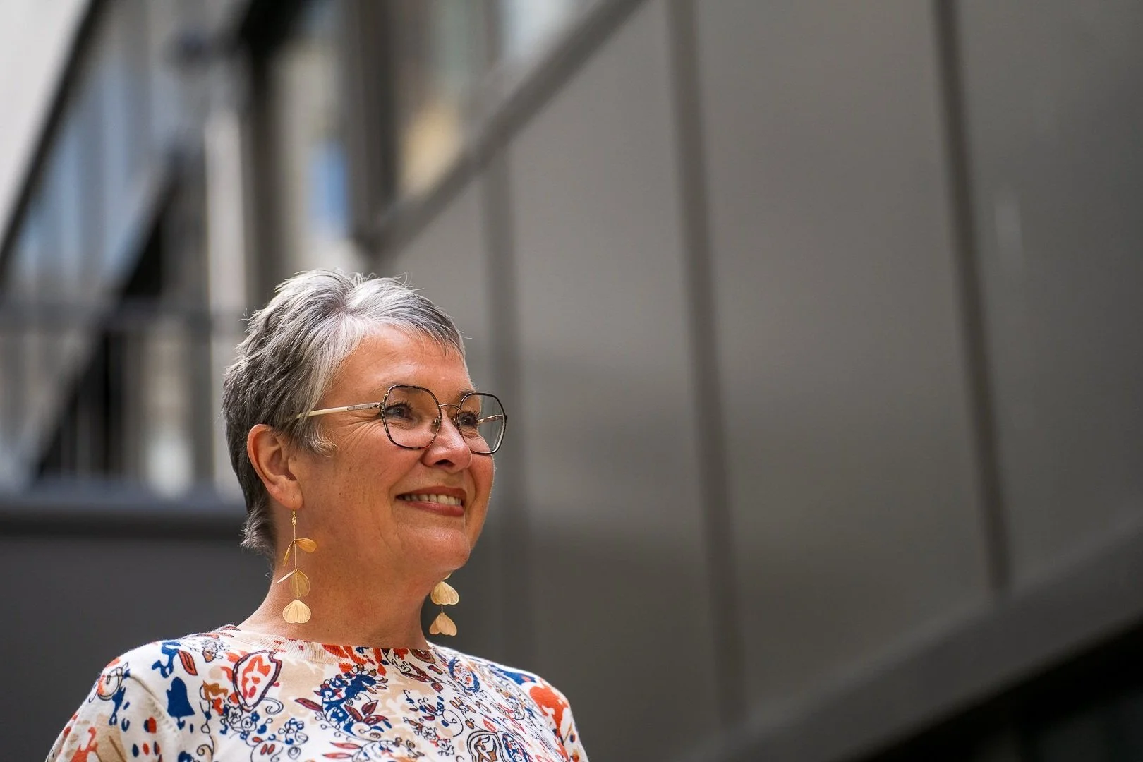 Corinne sourit dans un bâtiment moderne.