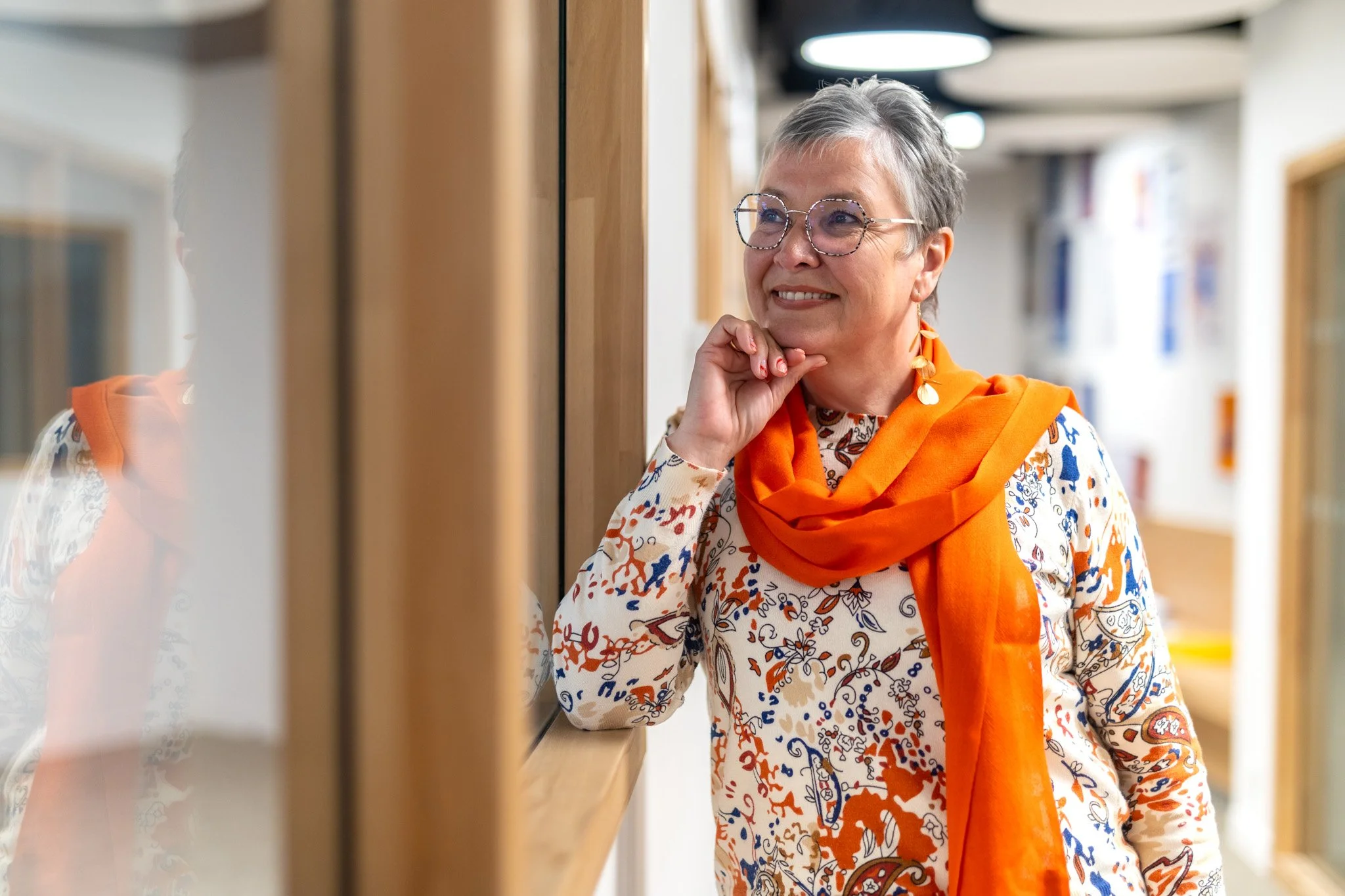 Corinne sourit tout en se tenant près d'une fenêtre dans une galerie d'art ou un musée.