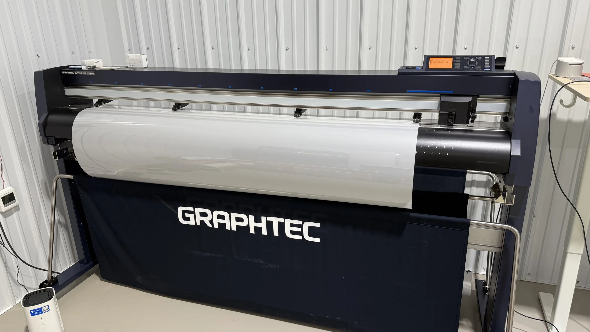 Large digital cutting machine with the brand name GRAPHTEC visible, set up for printing or cutting material in an industrial setting.