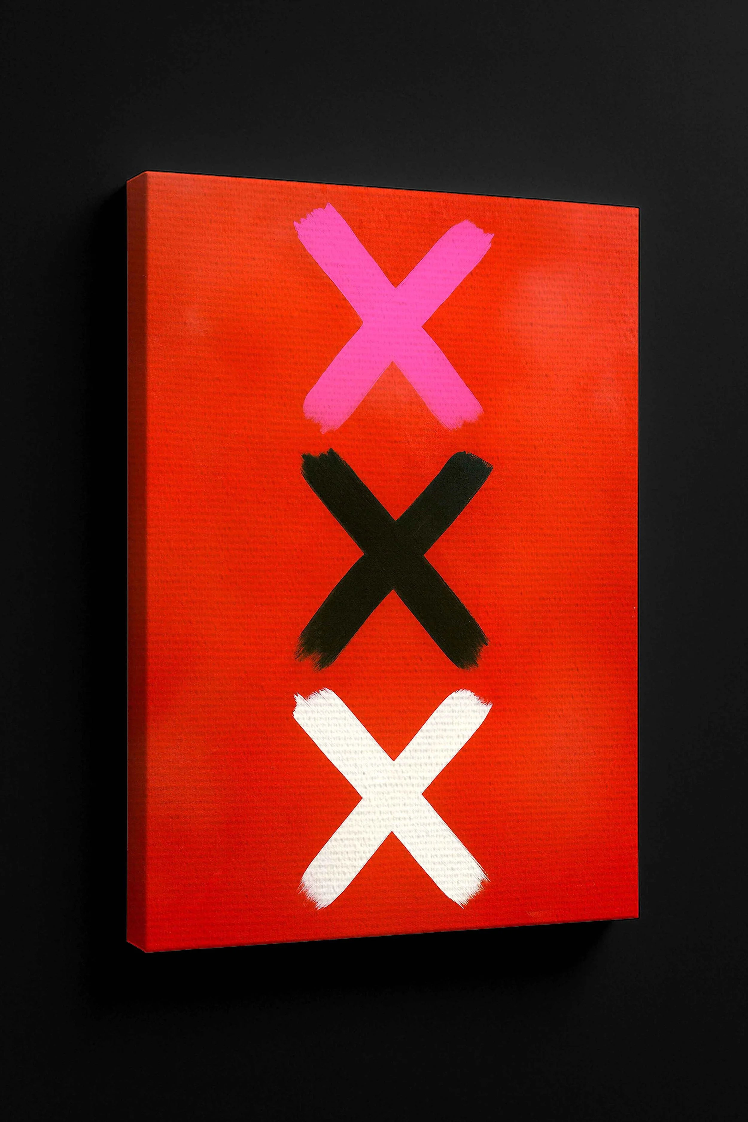 Close-up angled canvas of modern wall art featuring three bold X marks in pink, black, and white on a red background, displayed against a black wall.