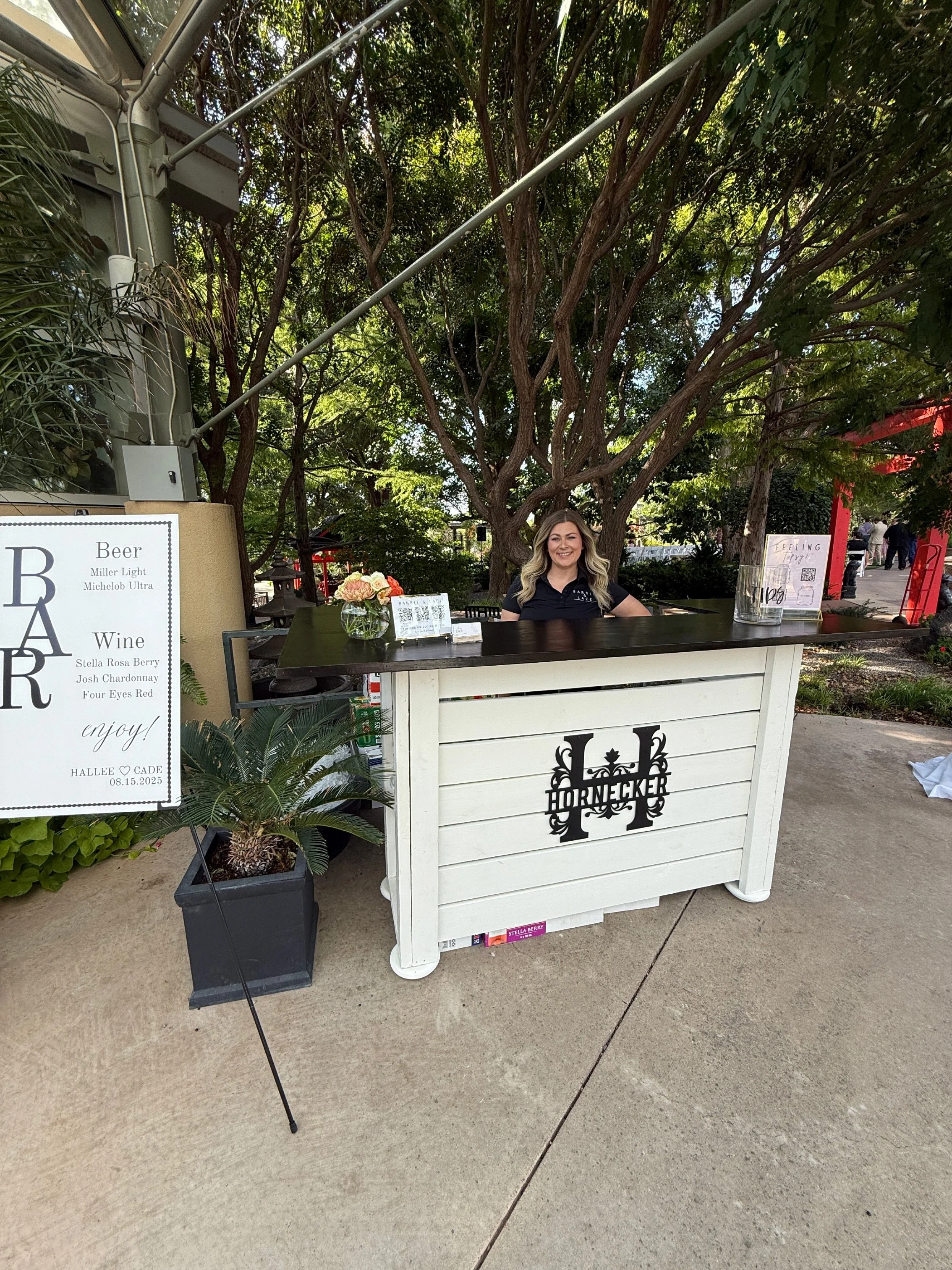 Woman staffing a Hornēcker beer and wine bar at an outdoor Amarillo botanical garden event.