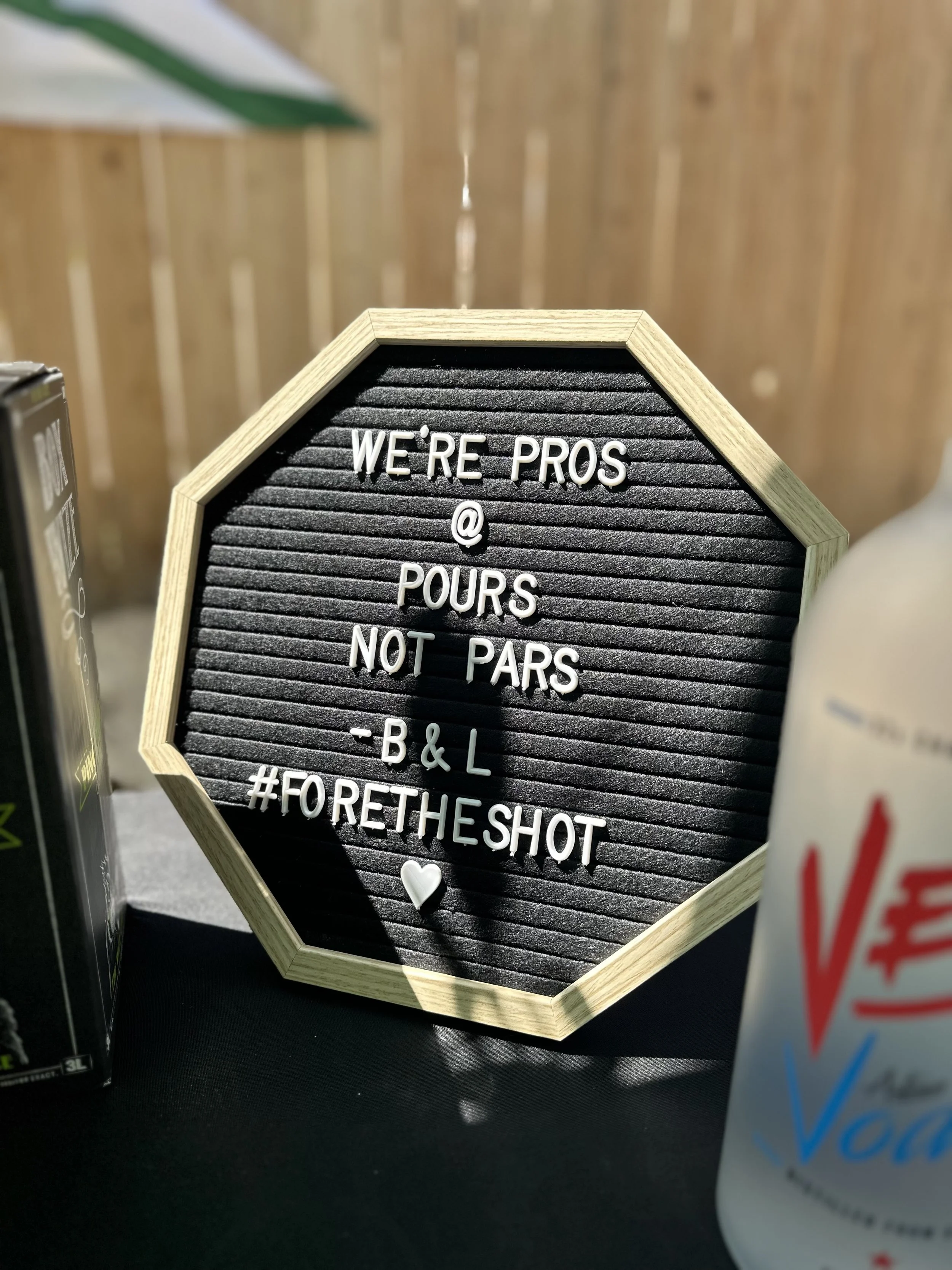 Hexagonal black felt letter board displaying “WE’RE PROS @ POURS NOT PARS – B&L #FORETHESHOT” with a heart symbol.