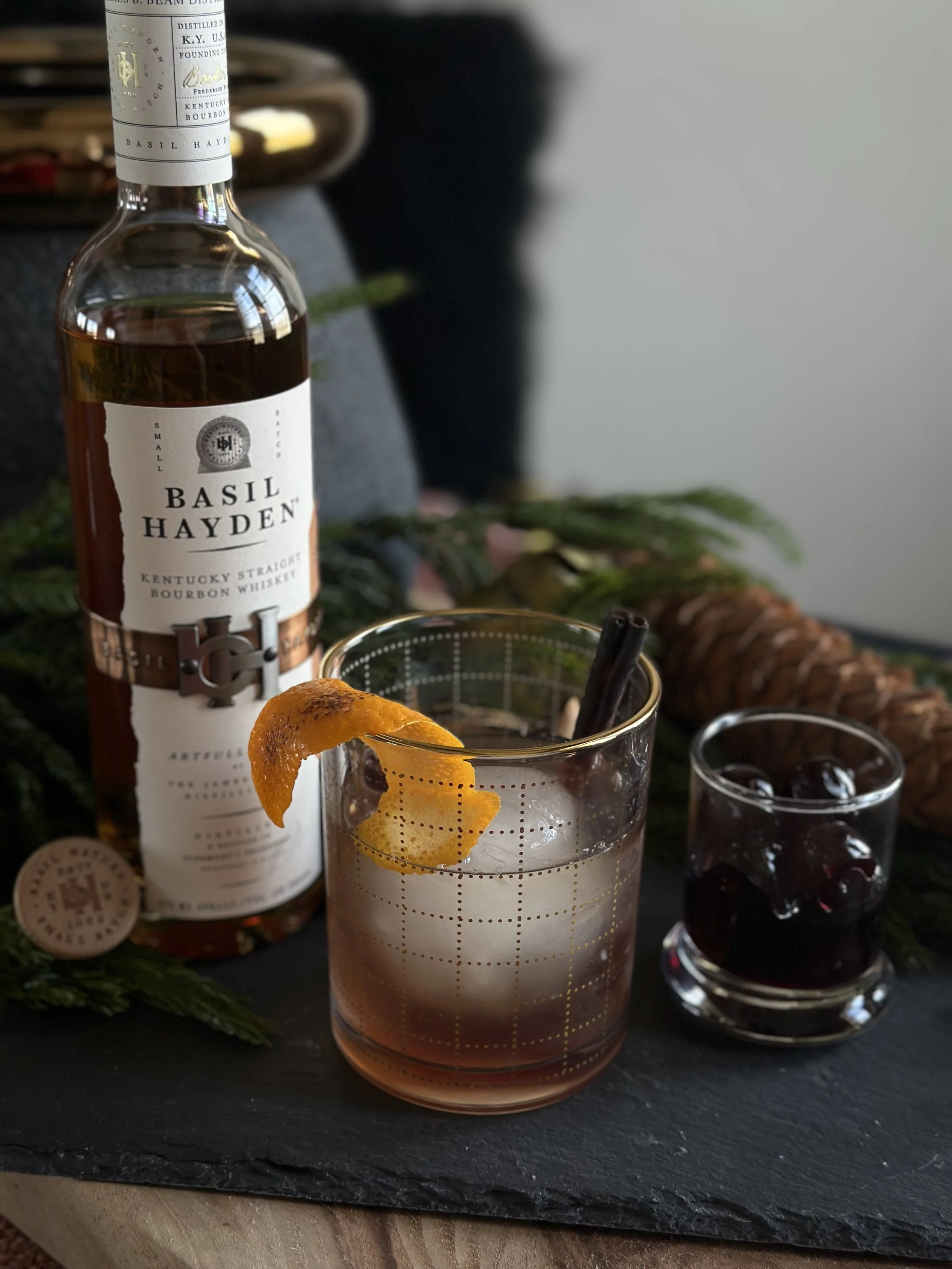Basil Hayden Kentucky straight bourbon bottle beside a stirred bourbon old fashioned cocktail garnished with an orange peel and cinnamon stick