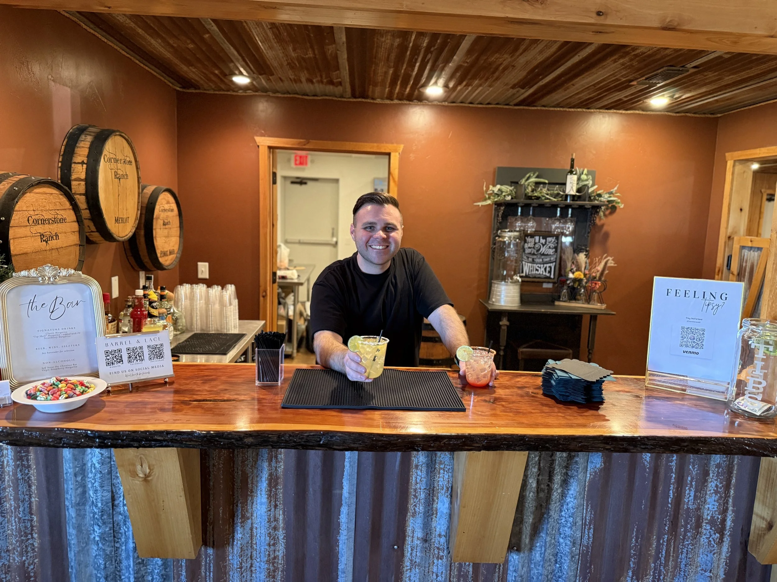 Bartender serving colorful cocktails at a rustic ranch-themed bar at Cornerstone Ranch in Amarillo with wine barrels and drink menus.