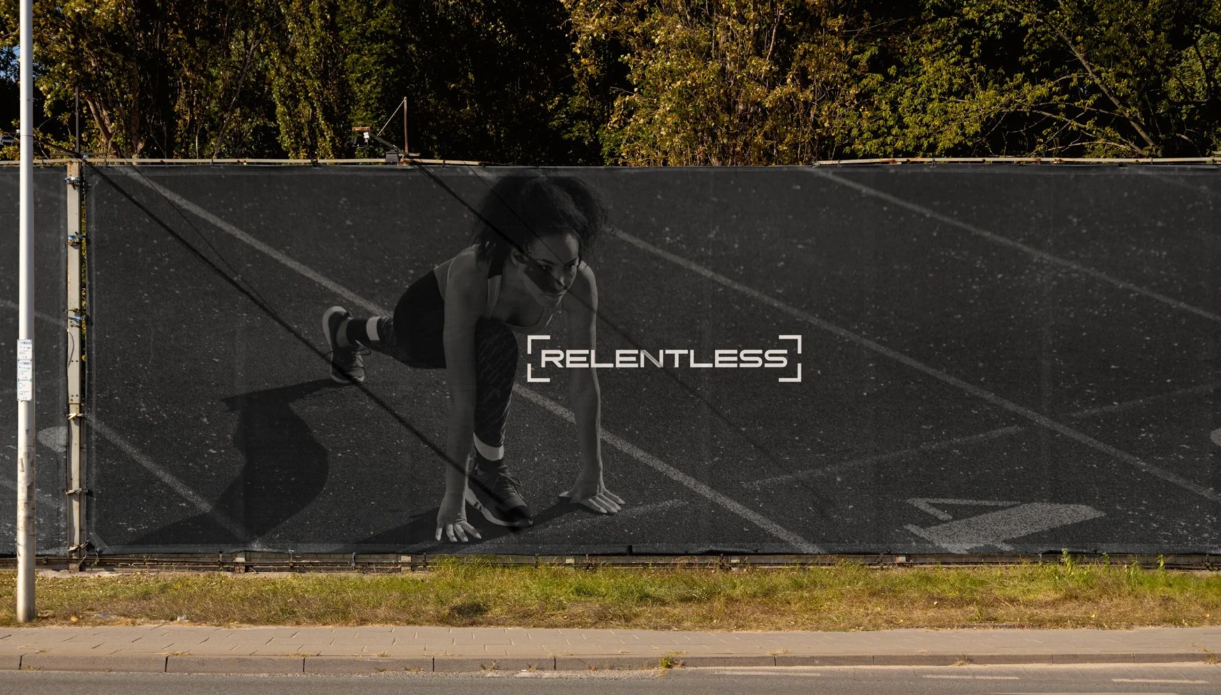 Outdoor fence banner displaying the Relentless brand over an athlete in motion, demonstrating how the identity scales across physical environments.