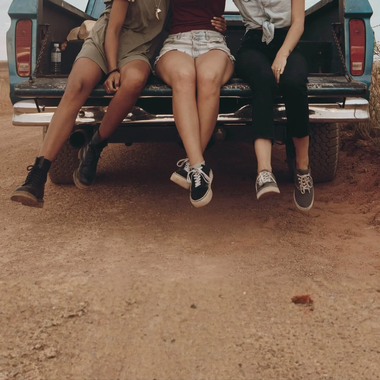 Three women sitting together on the back of a truck, symbolizing friendship, support, and shared life experiences