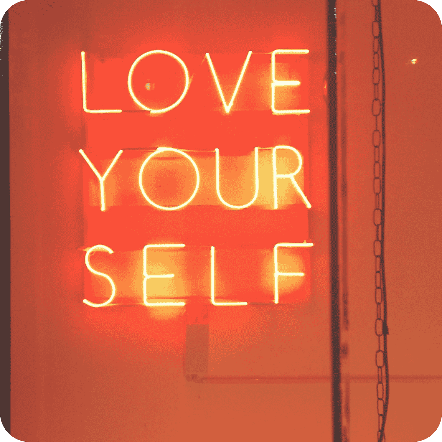 Glowing yellow neon sign reading “Love Your Self” against a red-orange background