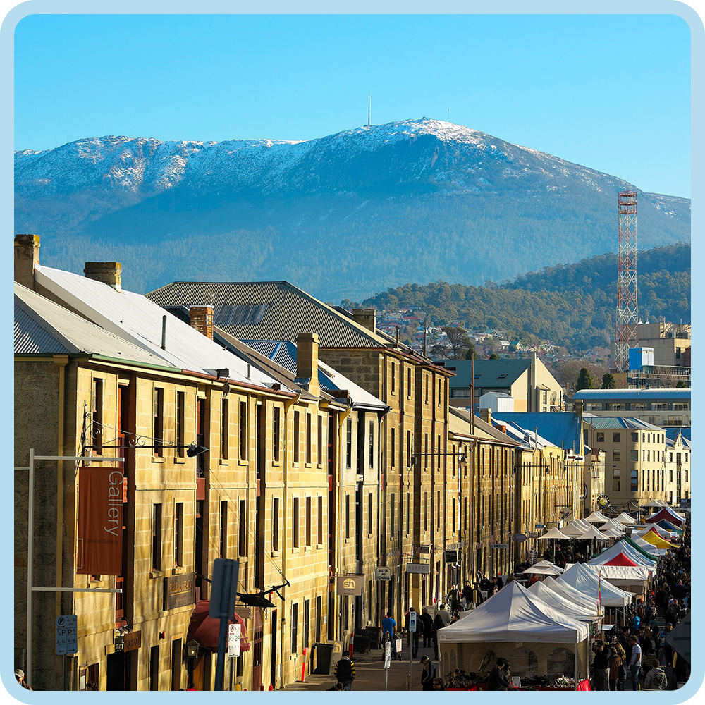 City street with market tents and historic buildings, mountain with snow in the background.