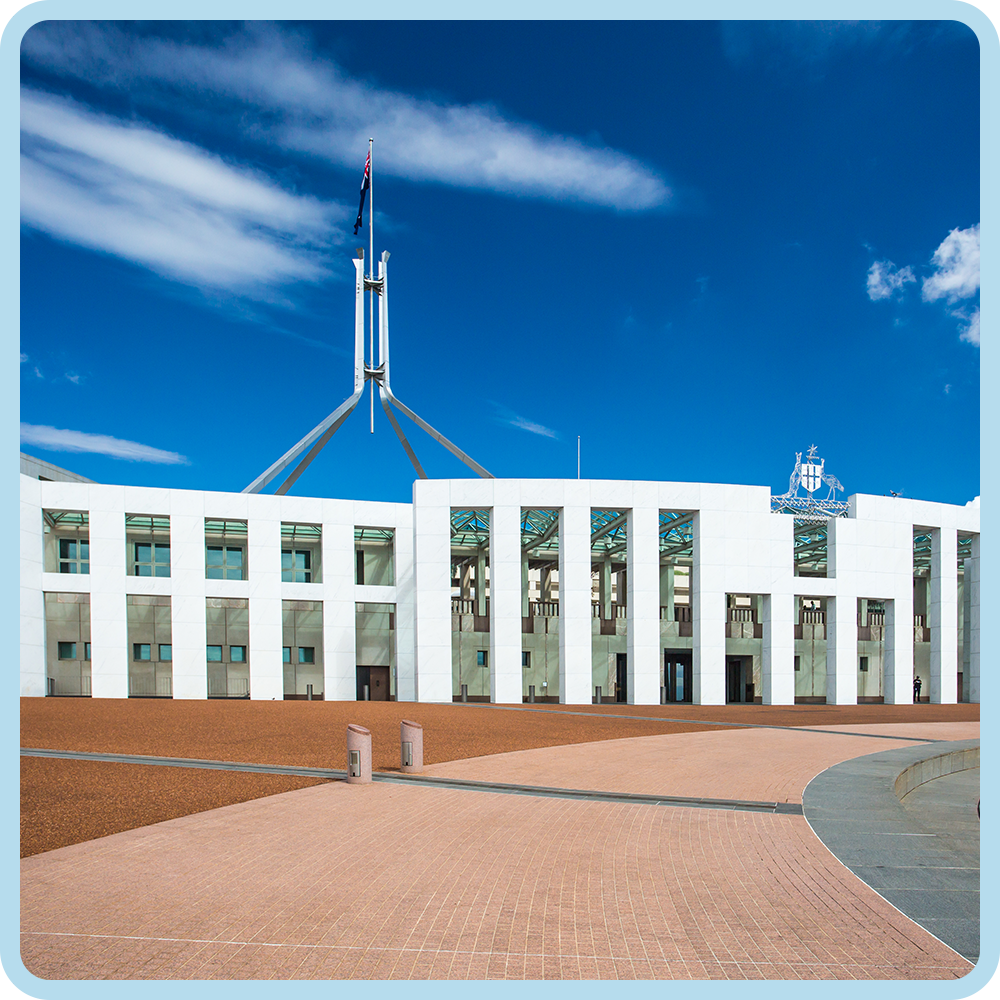 Front view of the Parliament House in Canberra, Australia with a clear blue sky, featuring white modern architecture and a flagpole with the Australian flag.