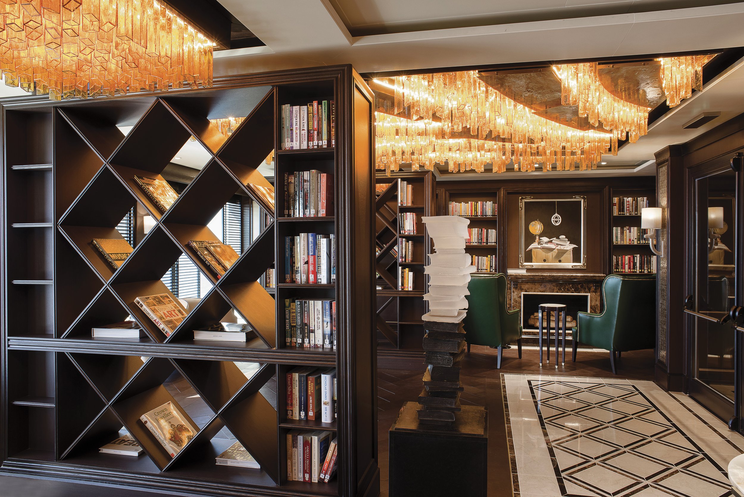 Interior of a library or study room with a dark wood bookshelf and modern golden chandeliers.