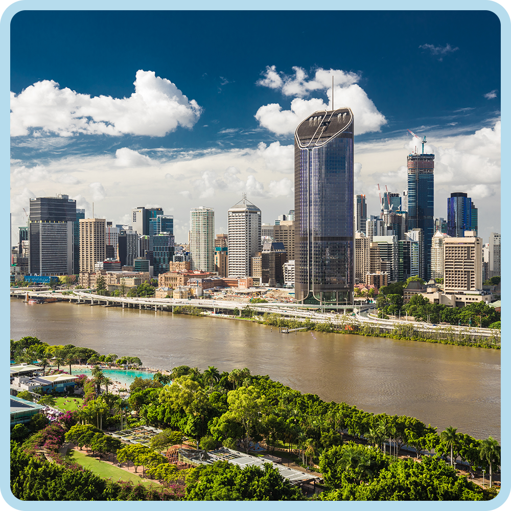 Skyline of a modern city with tall skyscrapers, a river in the foreground, and a park with trees and a pool area.