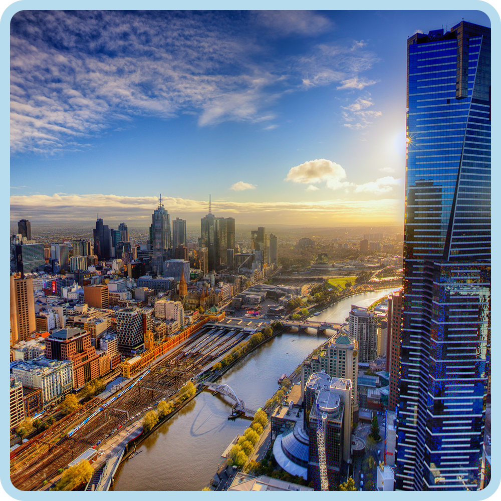 Aerial view of a city skyline at sunset with tall skyscrapers, a river, bridges, and a mix of modern and historic buildings.