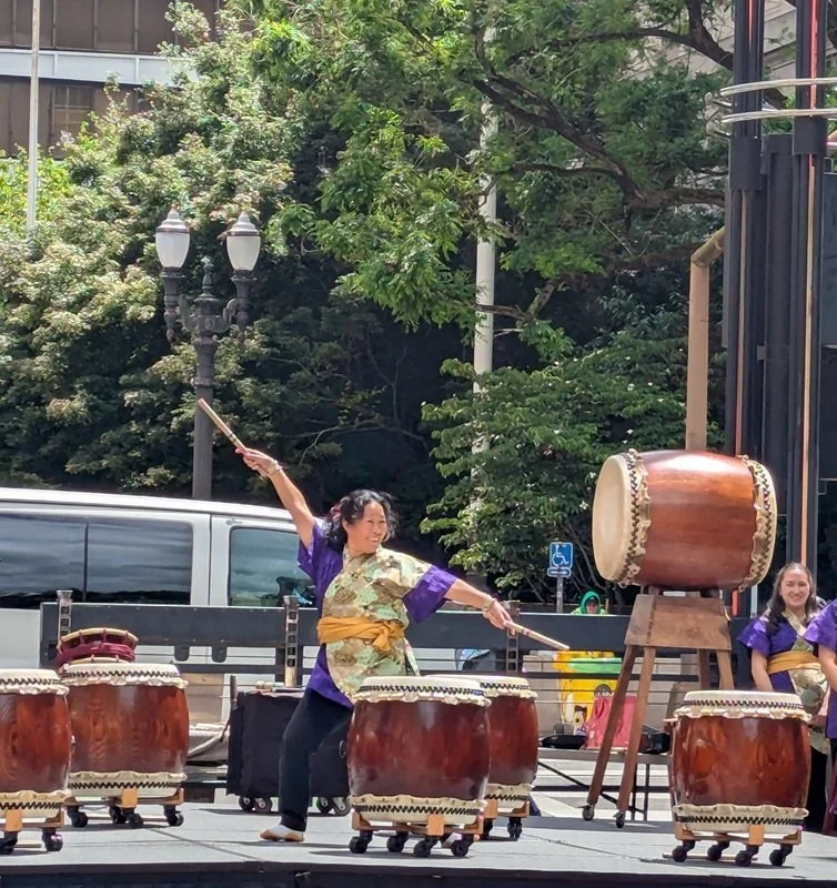 A taiko performer poses behind a drum with arms extended