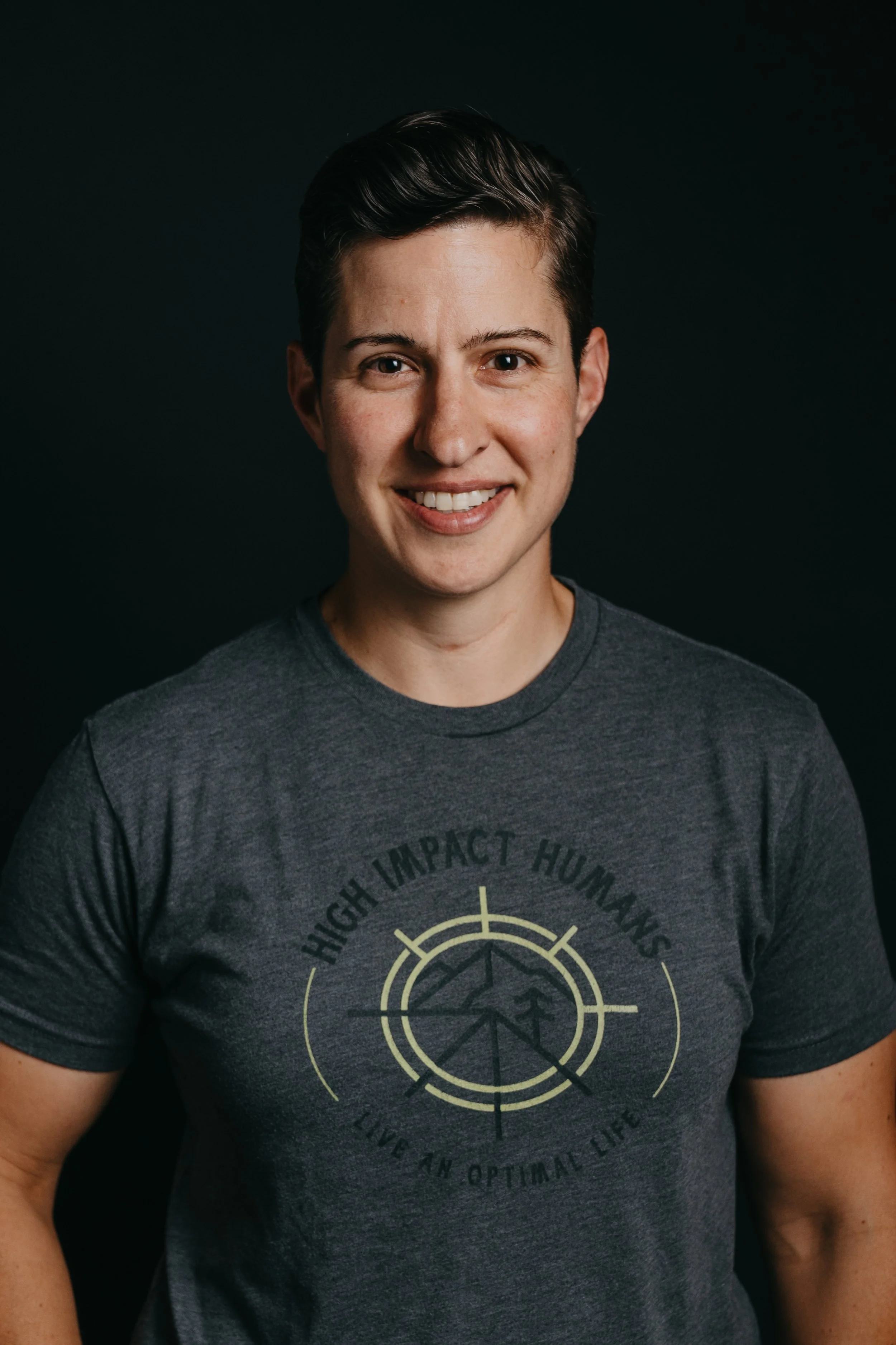 Woman with short hair smiling, wearing a grey t-shirt with "High Impact Humans" printed on the front