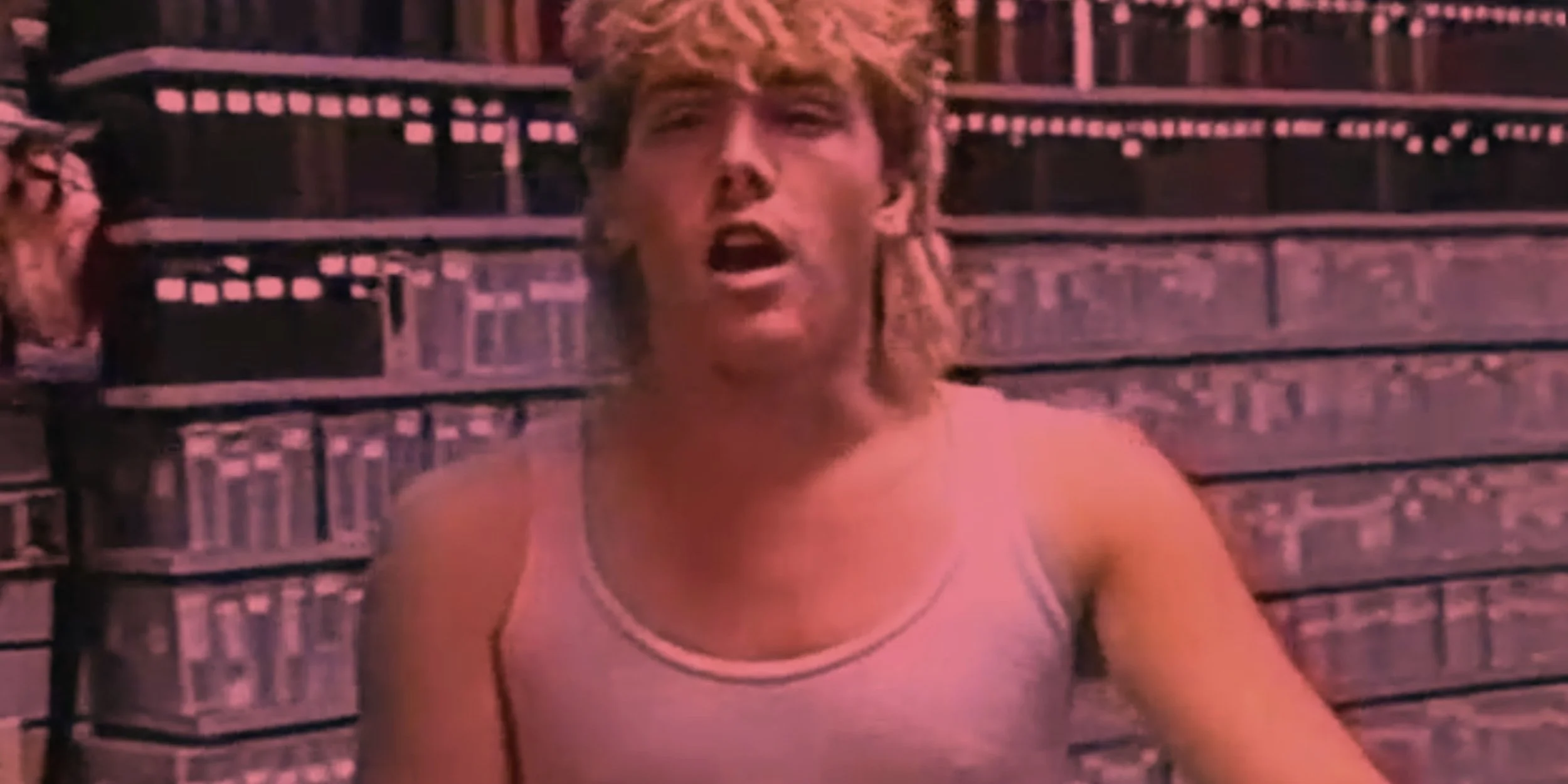 A shirtless man with dark hair and a beard, standing against a plain background.