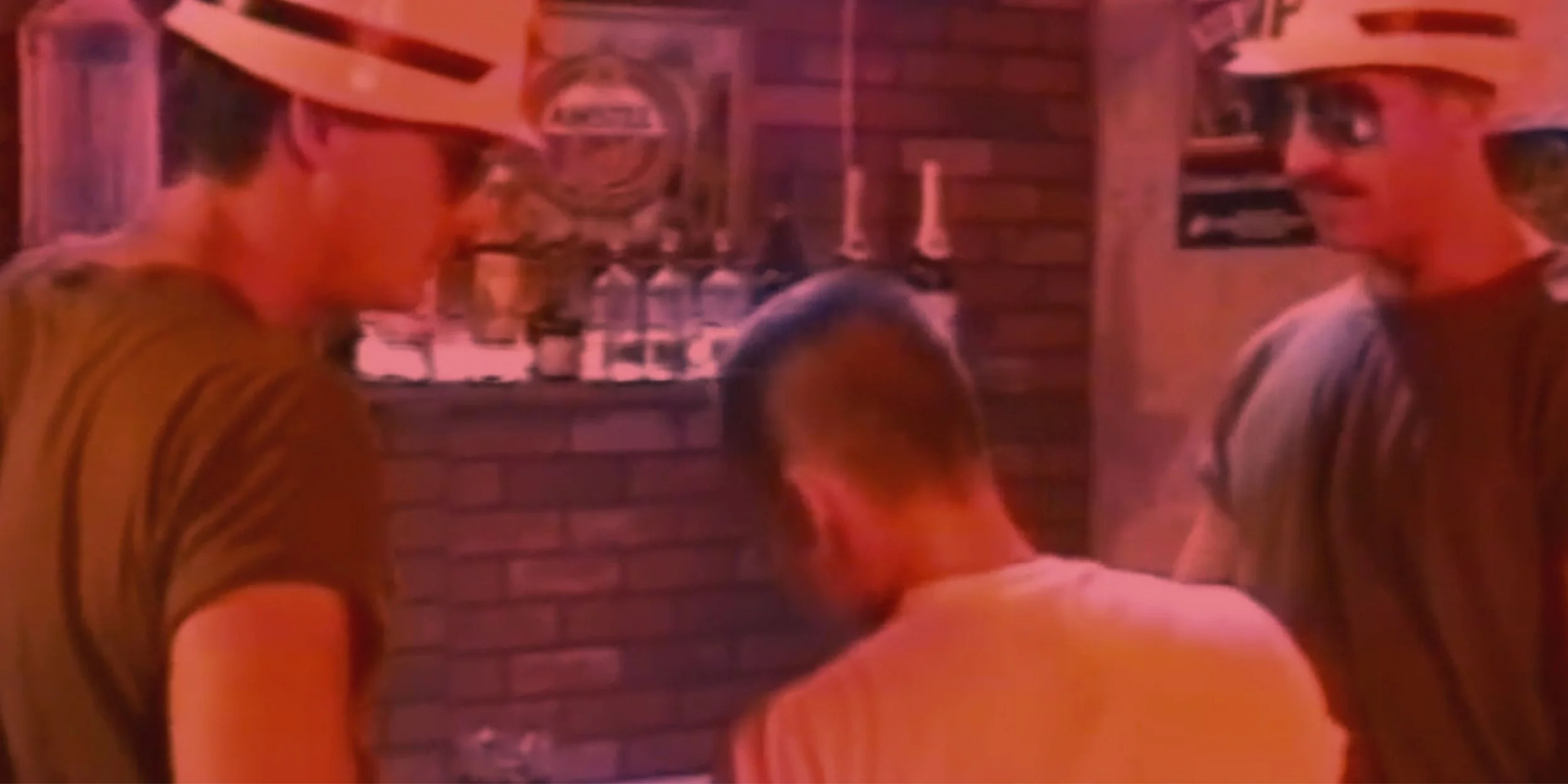 A smiling man with a beard submerged in a hot tub or pool, illuminated by pink or purple lighting, showing his upper body and part of his face.