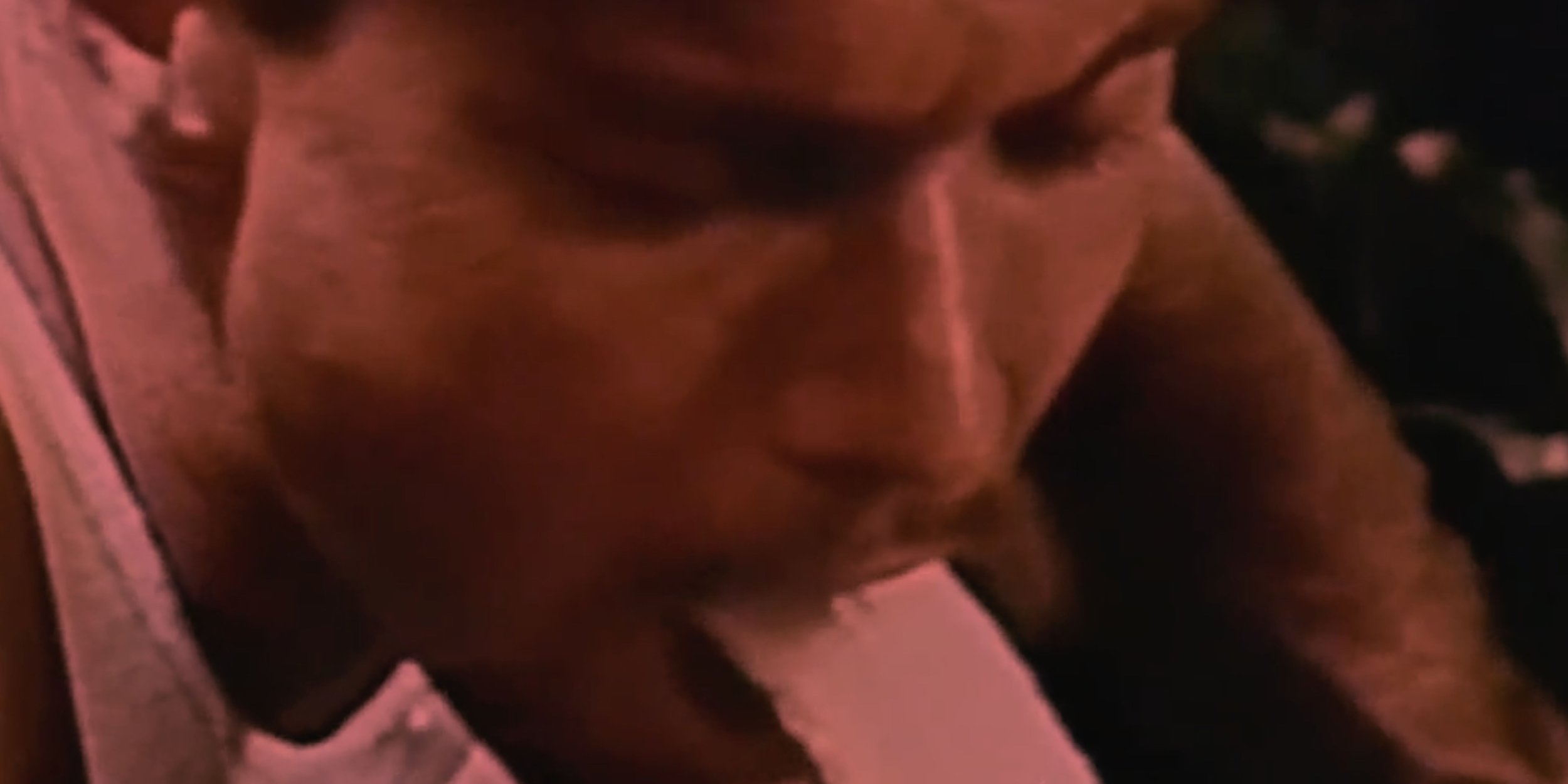 Close-up of a muscular person with dark skin, sitting with their arms crossed over their chest, wearing a pink garment.