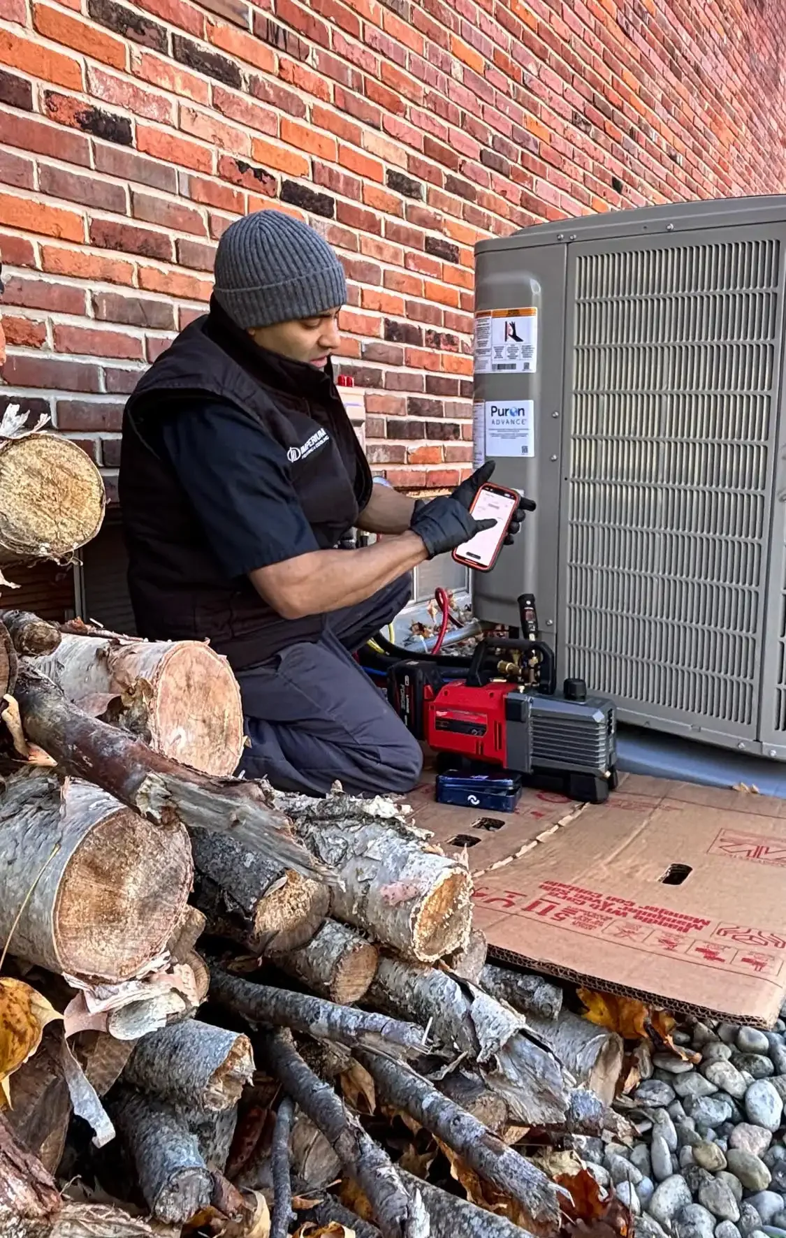 HVAC technician using a smartphone app to monitor a Milwaukee vacuum pump while commissioning a Bryant Puron Advance air conditioning unit.