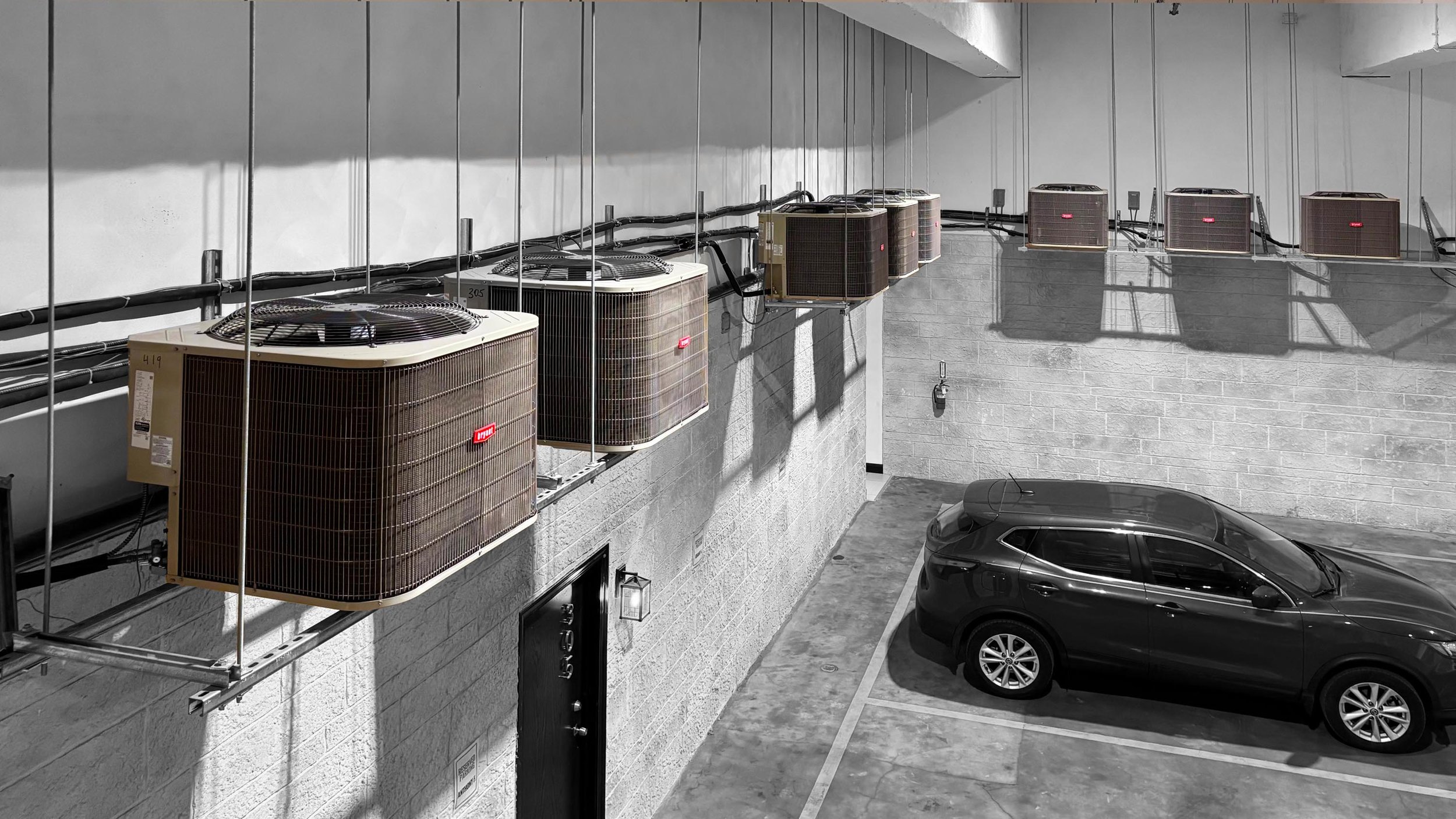 A row of industrial Bryant HVAC condenser units mounted high on a concrete wall above a parking garage, demonstrating a large-scale commercial climate control installation.