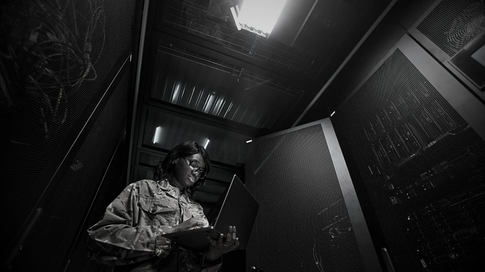 A woman wearing military camouflage uniform and glasses working on a laptop in an OmniGaza data center that powers and secures data for the United African Defence Force (UADF) by The Ndege Group, Africa's Sovereign Development Trust