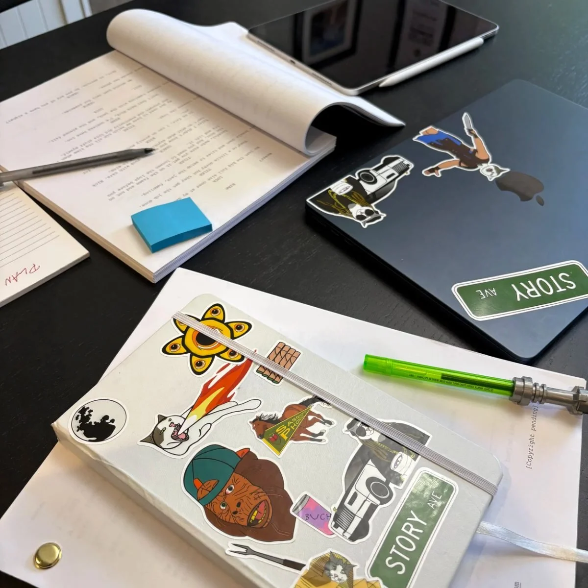 A desk with papers, stickers, a laptop with stickers, a pen, and a green highlighter.