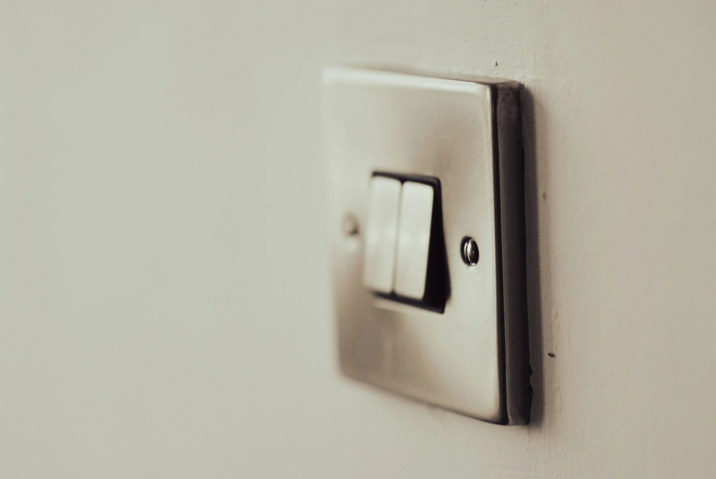 Close-up of a metallic light switch on a white wall, with two toggle switches in the off position.