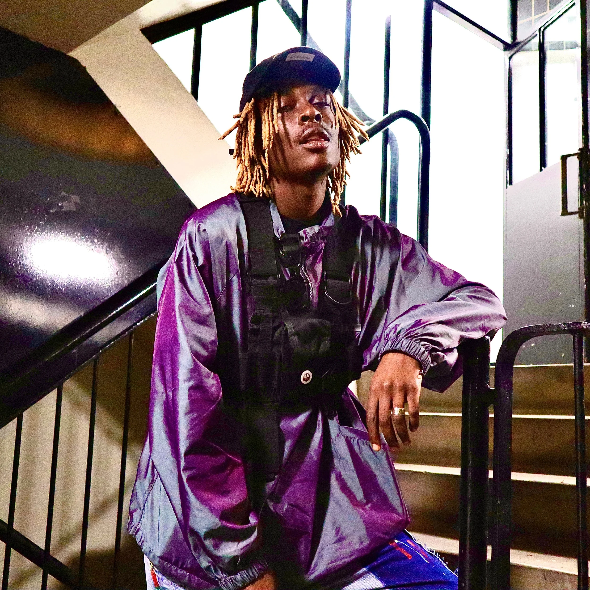 Young Gstar in a purple jacket and cap standing on a staircase in a well-lit indoor setting.