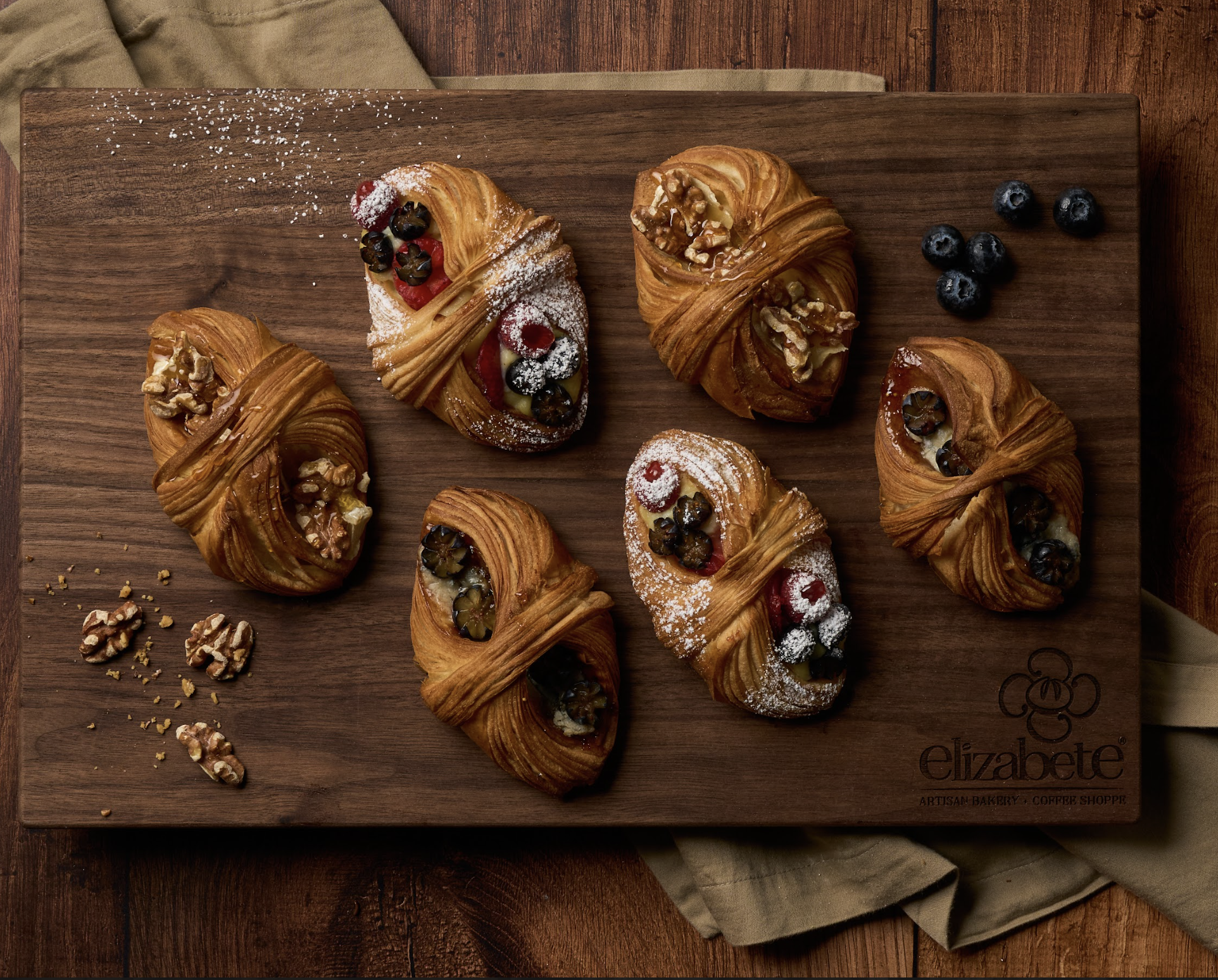 Multiple croissants are placed on a board, flaky and chocolate filled with a warm town of brown. 