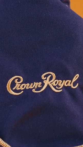 A warmly lit GIF showing different angles of a Crown Royal rum, it ends with a front shot and small drink glass being pushed into frame.