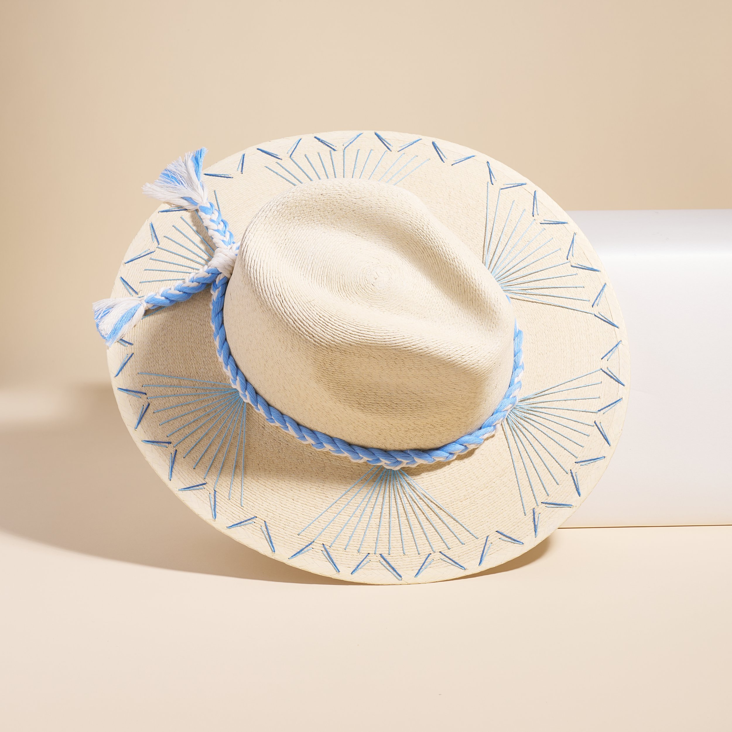 Cream colored stetson with baby blue accents and a small bow, tilted on a white block, top of the hat facing the audience.