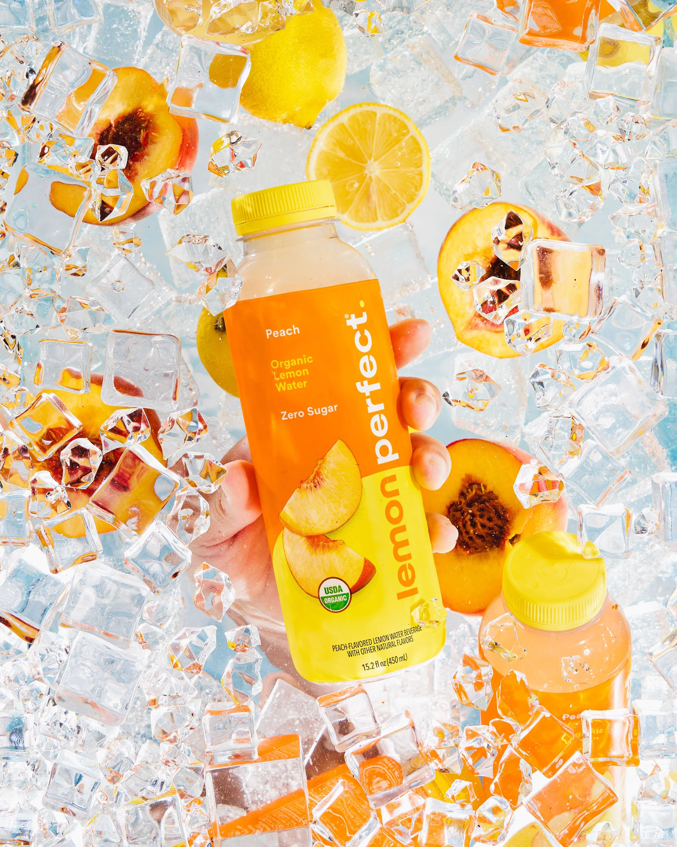 A refreshing Peach flavored drink from Lemon Perfect, submerged in ice with fruit and a hand pulling out the bottle.