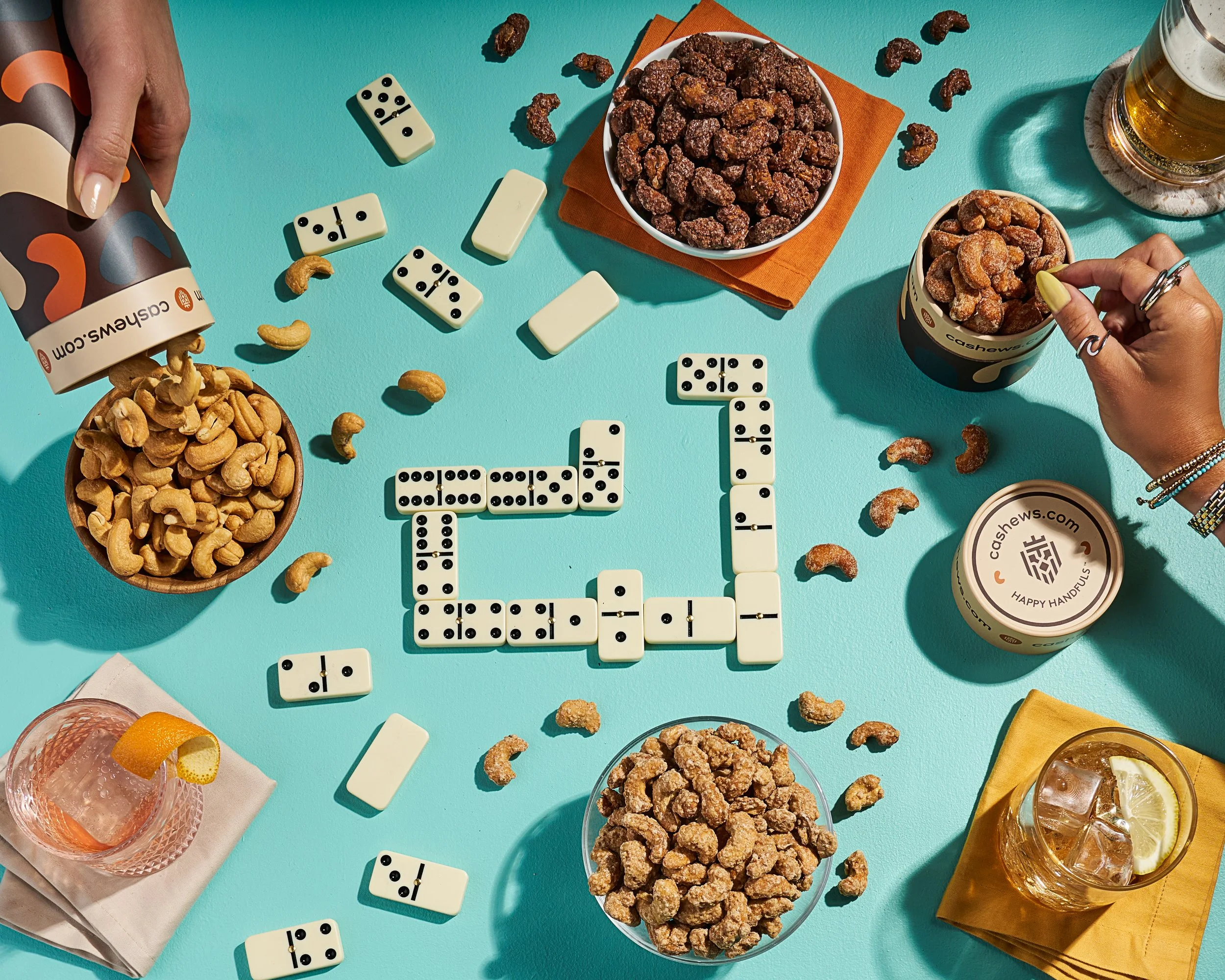 A spread of gourmet nuts, sweet treats, and cocktails set around a domino game for the perfect gathering vibe for Caramels.