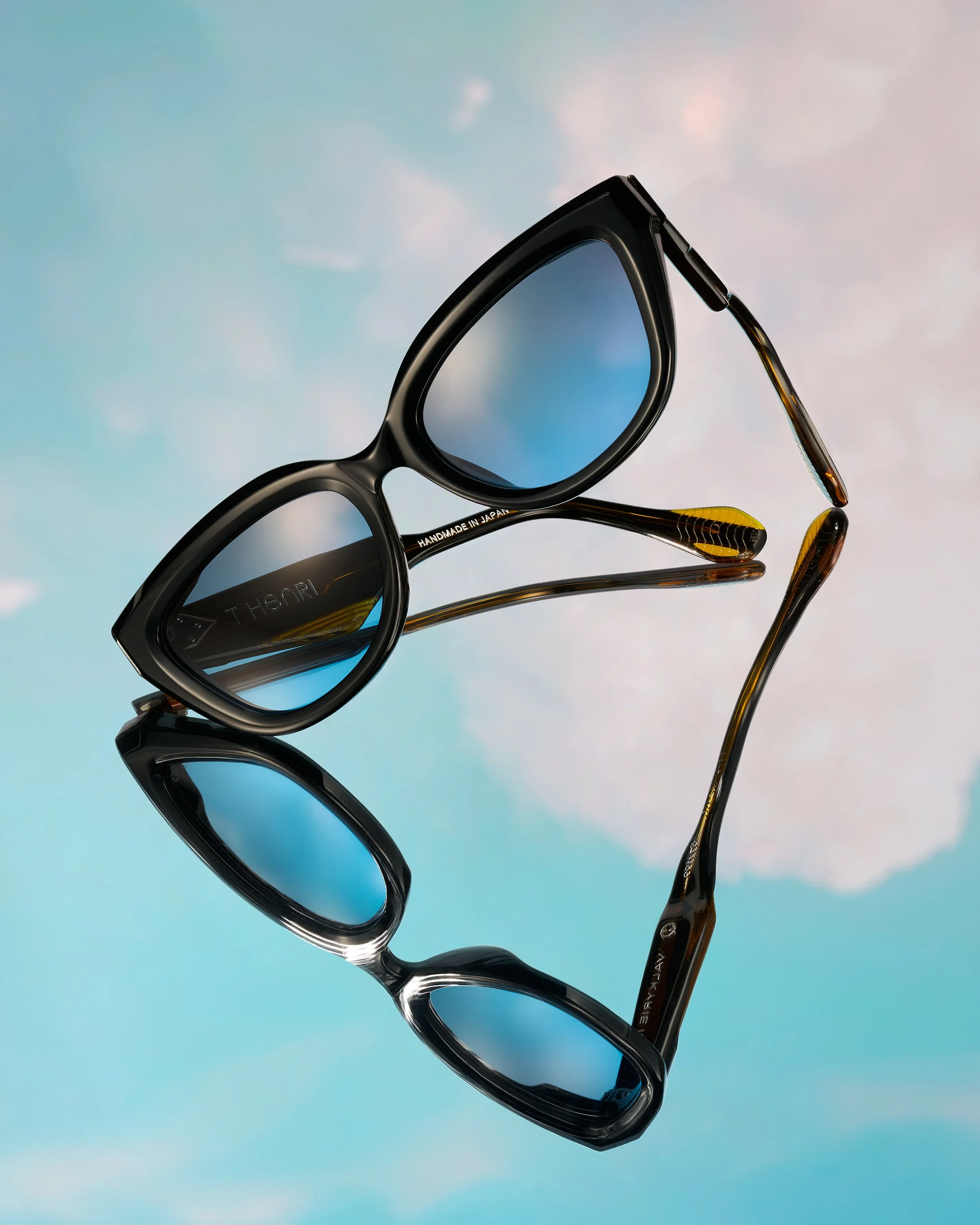 Luxurious T-Henri shades are placed on an angle on a sky backdrop, with light blue lens