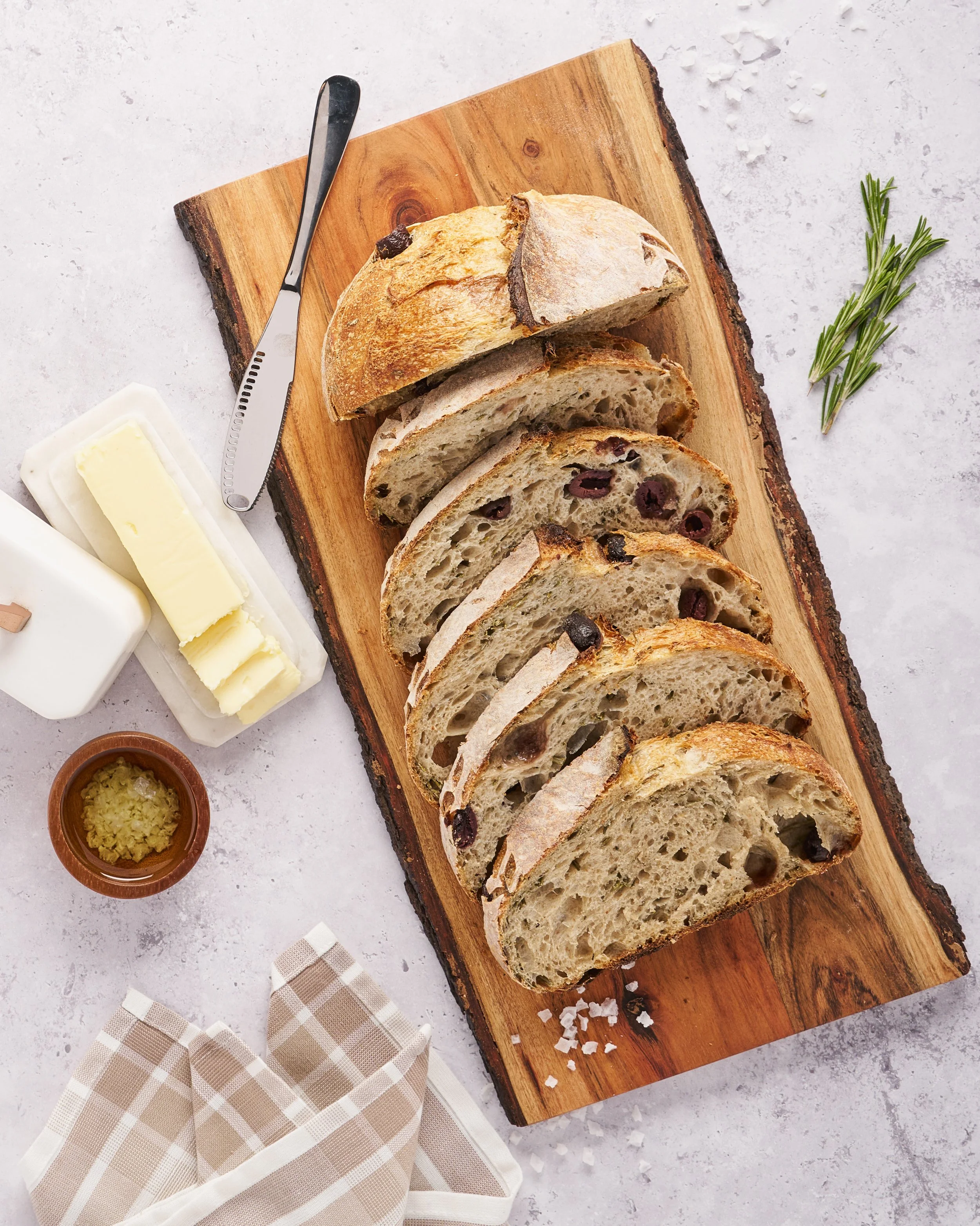 A loaf of bread has been sliced into multiple slices on a cutting board with a butter knife laying on its side and a few sticks of butter complimenting the board. 