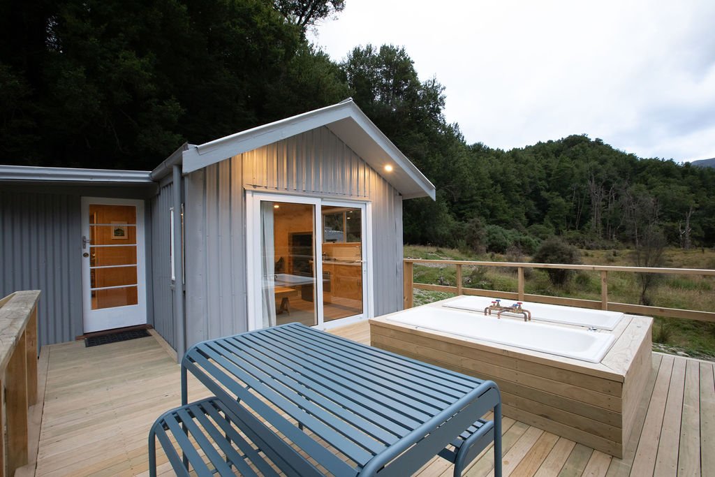 Outdoor deck with hot tub, metal table, and view of forested hills at dusk