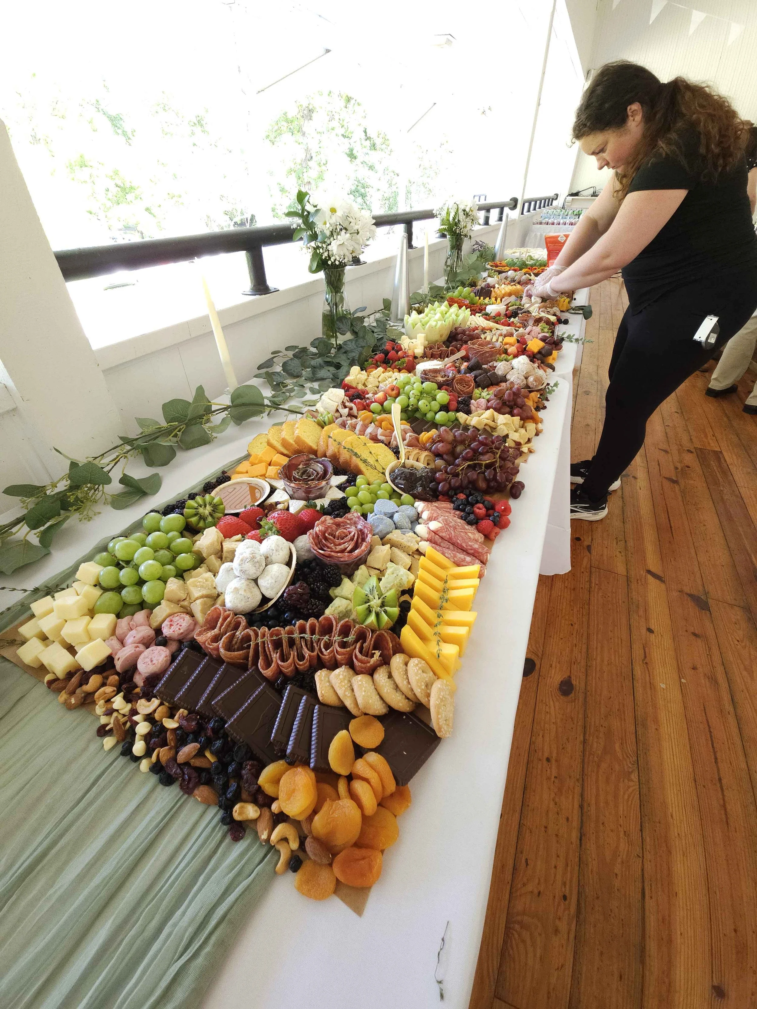 A long table charcuterie grazing table displaying an assortment of cheeses, fruits, and meats at a wedding.