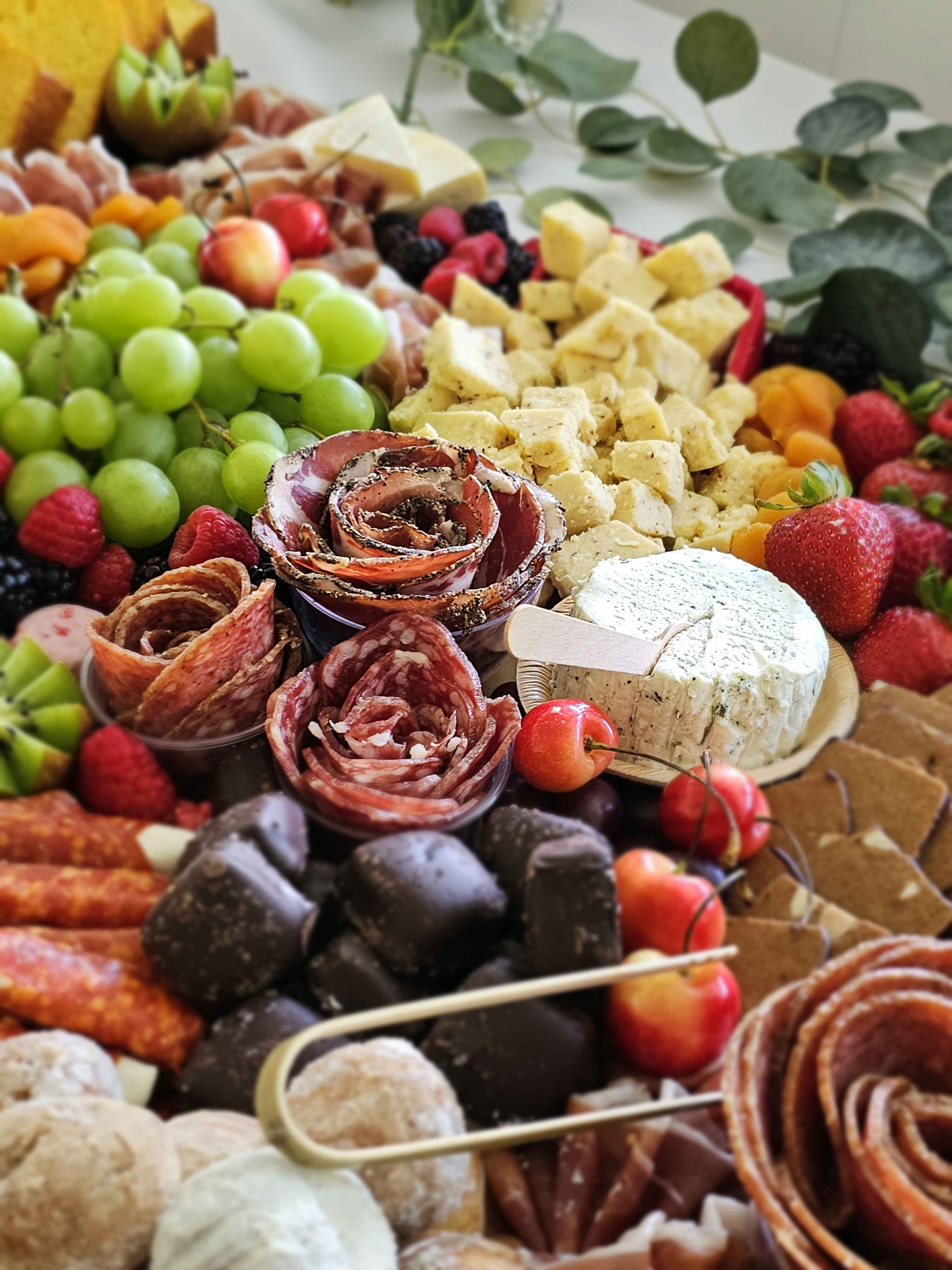 An assortment of cheeses, fruits, meats, and chocolates on display.