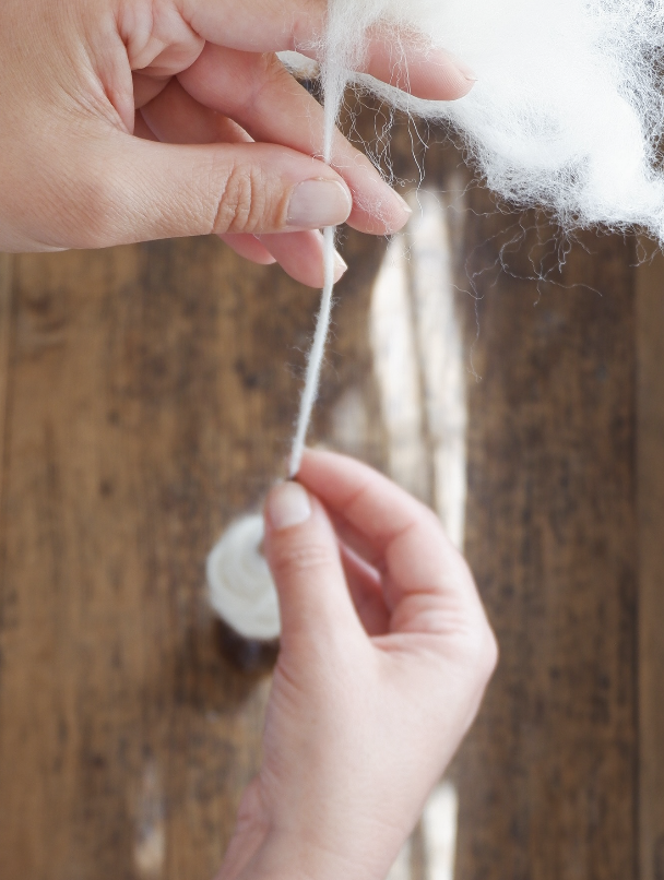 Hands twisting white yarn or wool into a strand in front of a wooden background.