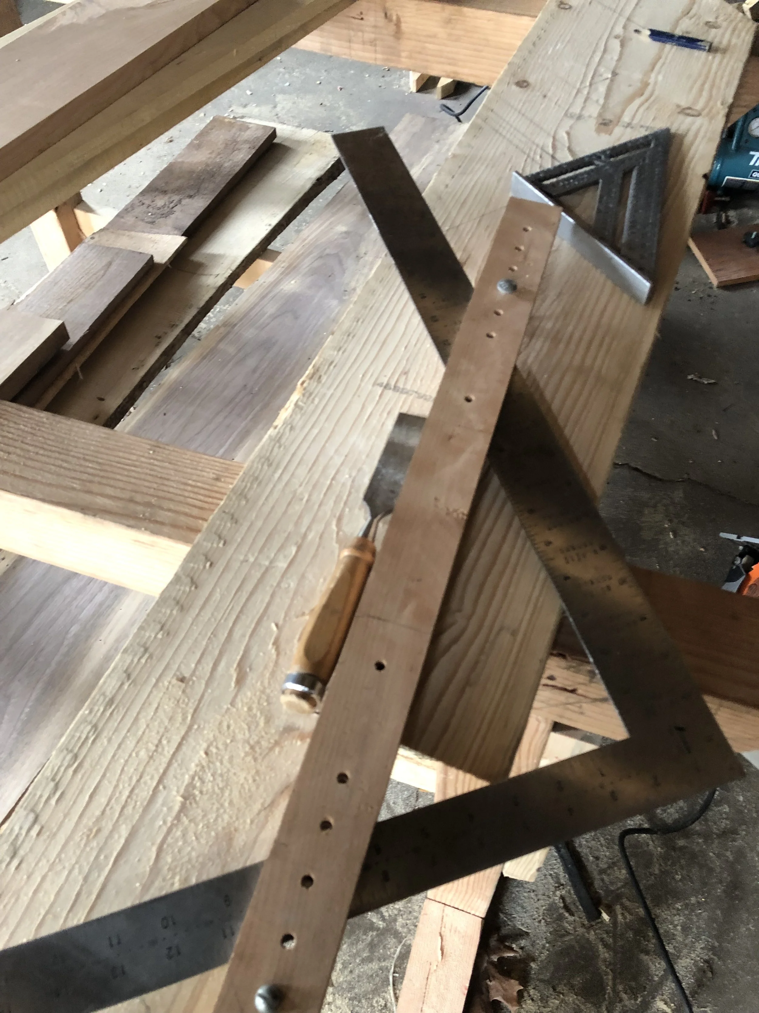 Woodworking tools on a wooden workbench, including a set square, ruler, chisel, and lumber pieces.