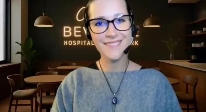 A woman wearing glasses and a headset with a microphone, smiling in a modern indoor setting, possibly an office or reception area.
