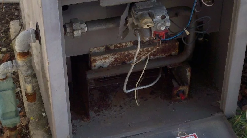 Close-up of a rusted and corroded industrial or HVAC unit with pipes and electrical wiring.