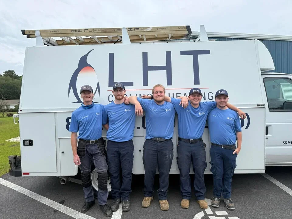 Five young men in blue shirts and hats standing in front of a white mobile unit with the logo and name 'LHT' on it, smiling and posing with their arms around each other.