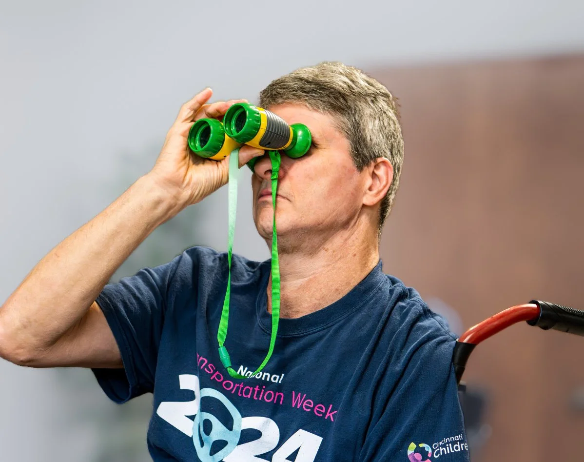 Man in a blue shirt looking through green and yellow toy binoculars.