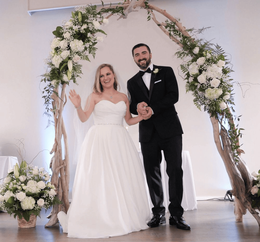 Bride and groom smiling under floral arch at wedding ceremony