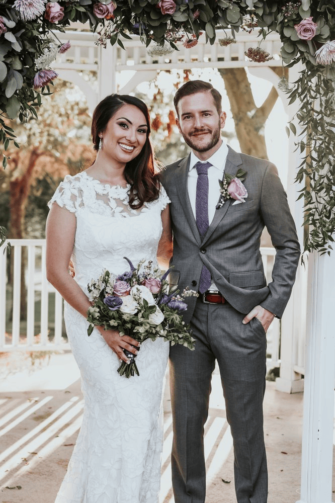 Bride and groom posing at a wedding under floral arch