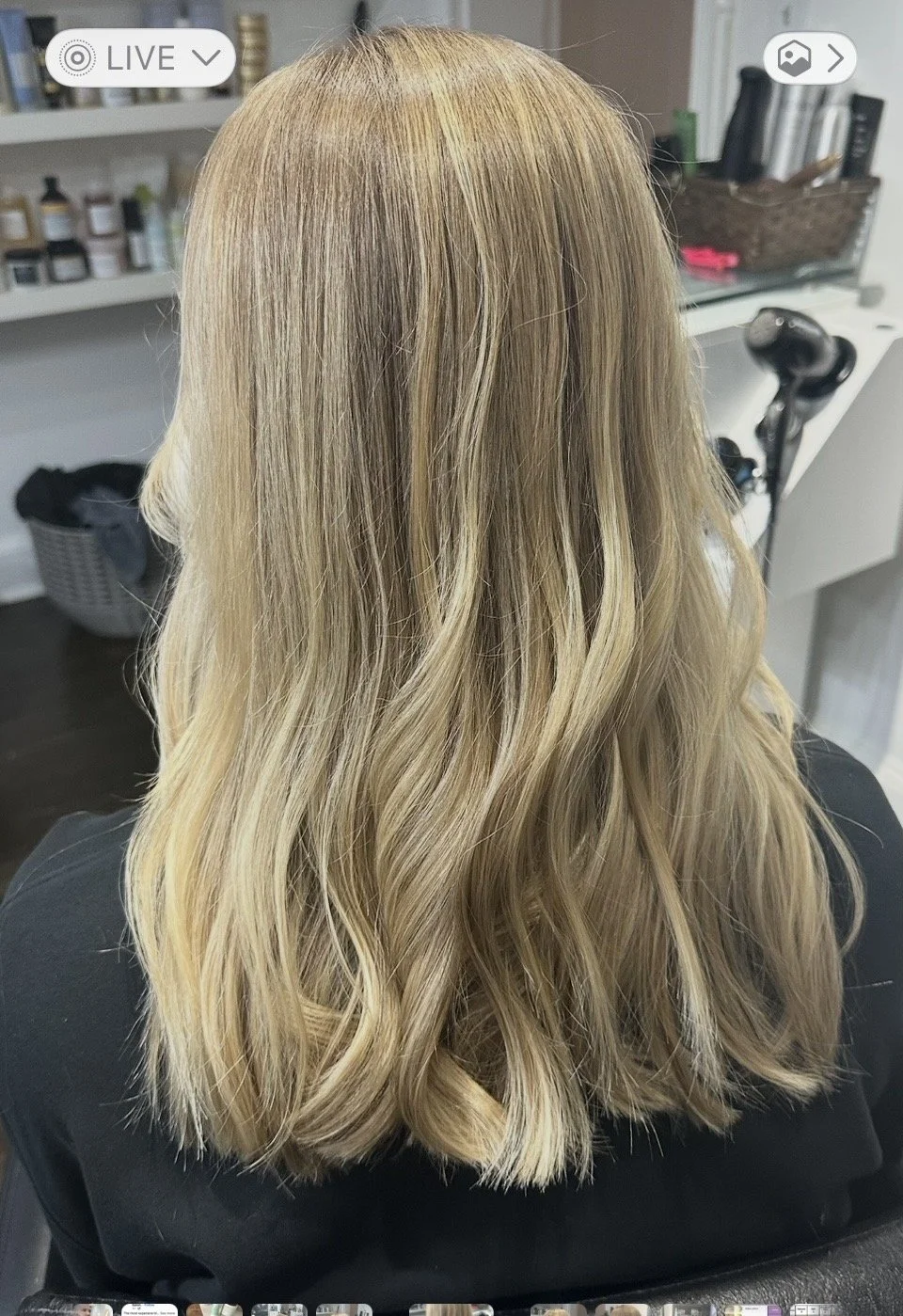 Back view of a person with long, wavy, blonde hair sitting in a salon chair.