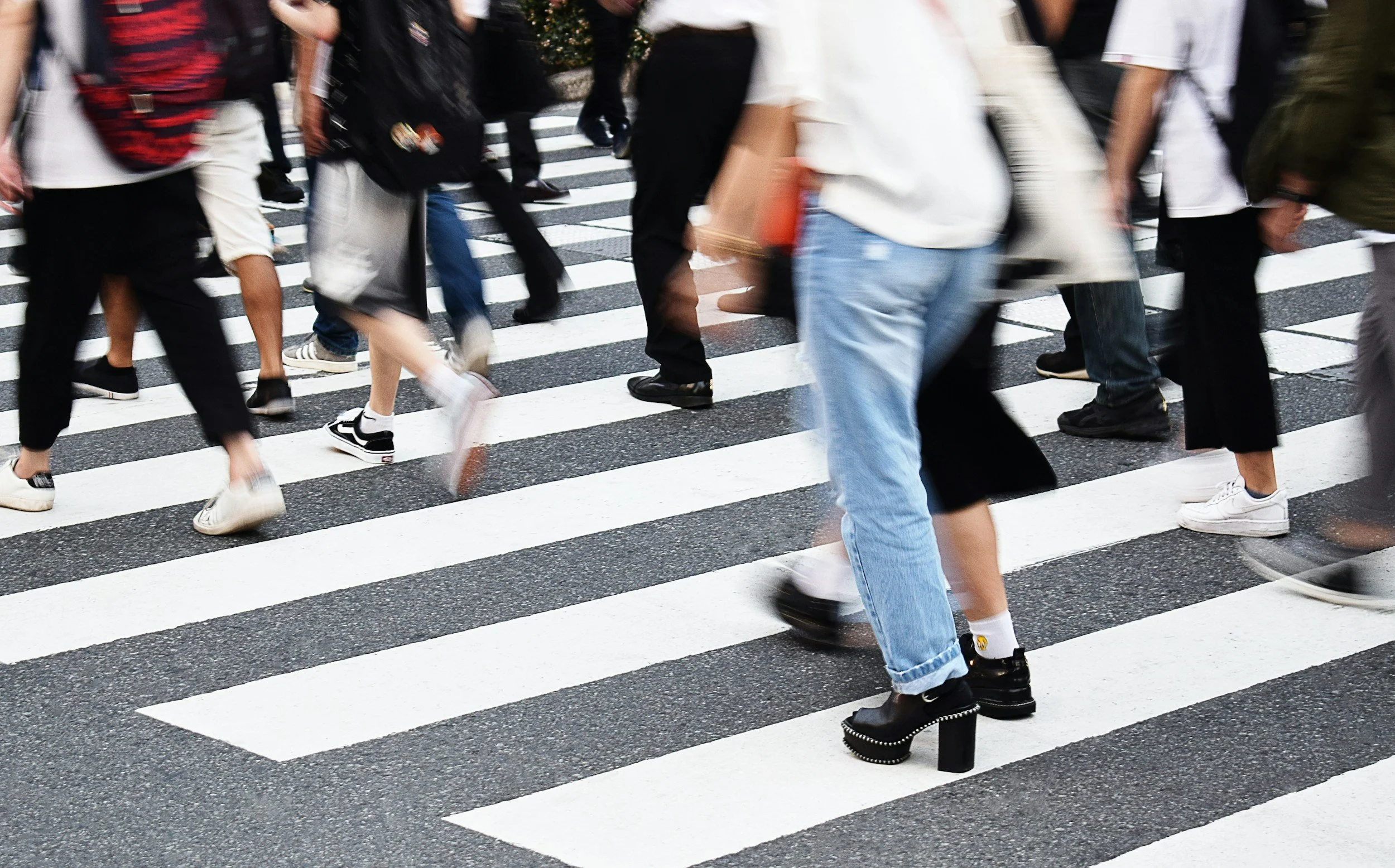 Many people walking across a black-and-white crosswalk on a city street.