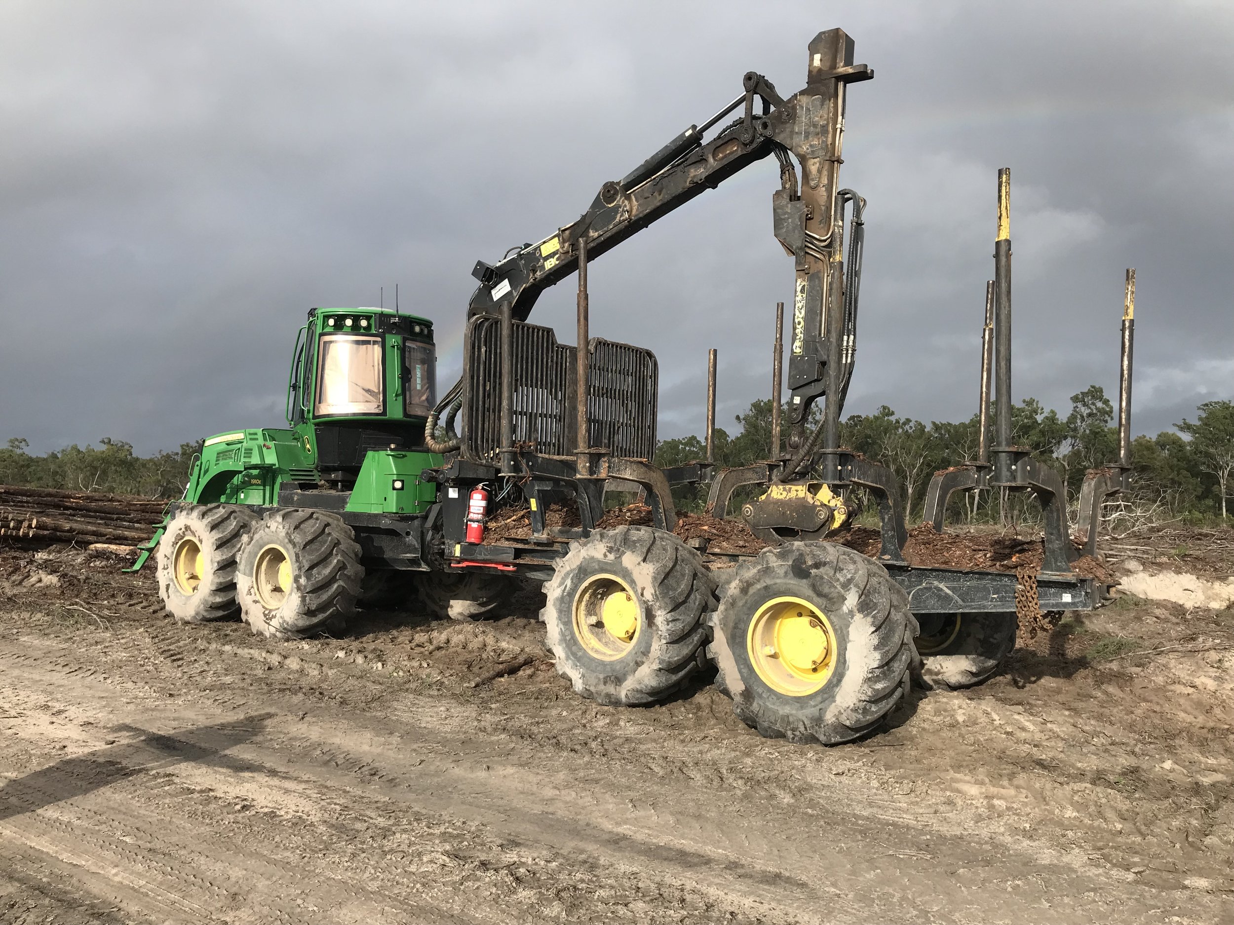 Forestry machine loaded with logs on muddy terrain, with cloudy sky background.