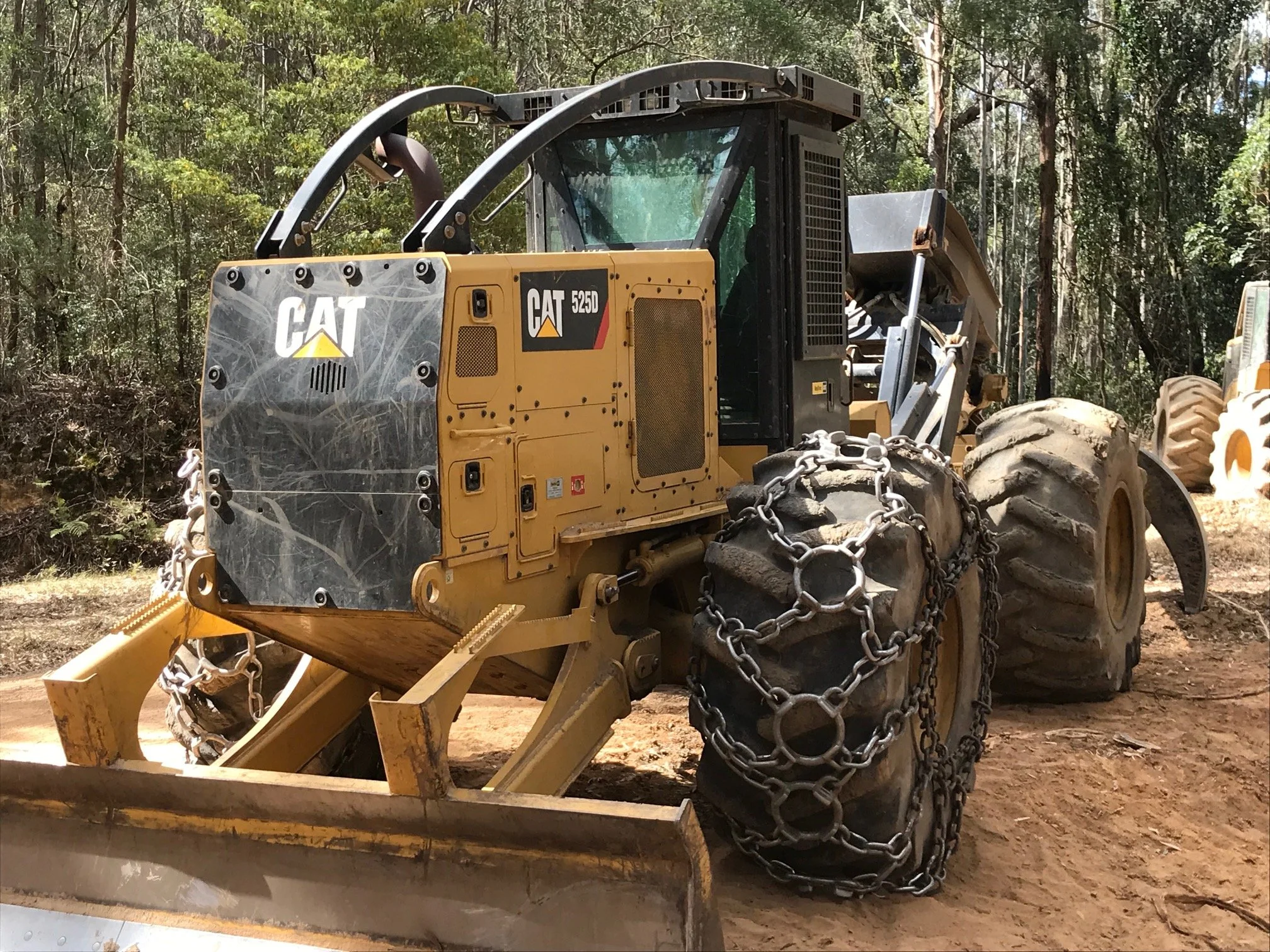 A yellow Caterpillar 525D skidder parked in a forest area, with chains on its front tires.