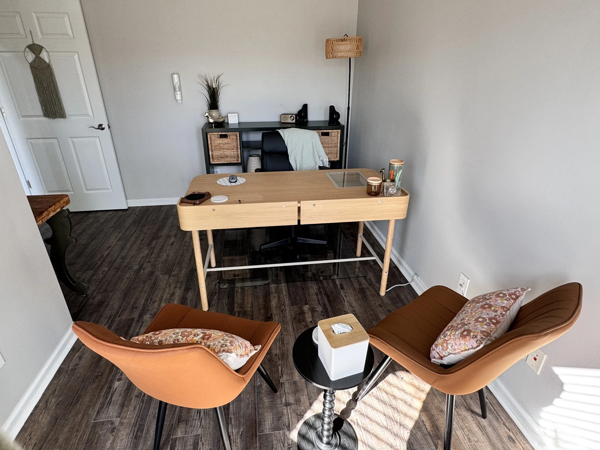 Cozy office space with a wooden desk, chair with a cushion, additional seating, and decorative elements such as a plant and lamp.